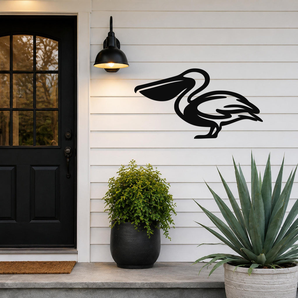 Black metal pelican wall art with a cutout silhouette, mounted on a white siding wall beside a front door and potted plants.