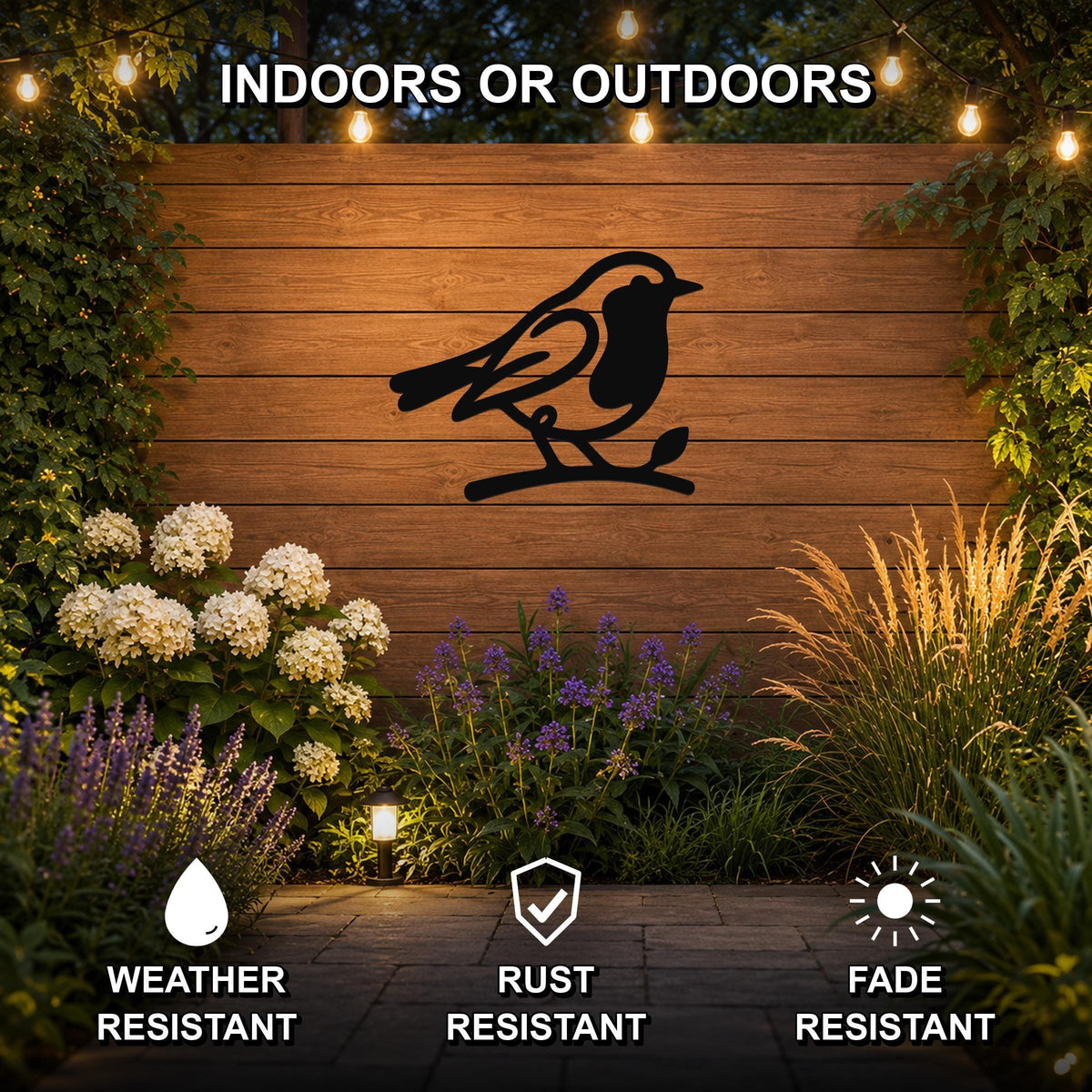 Black metal robin wall art silhouette perched on a branch, mounted on a wooden outdoor wall above a garden with flowers and string lights, weather resistant, rust resistant, fade resistant.