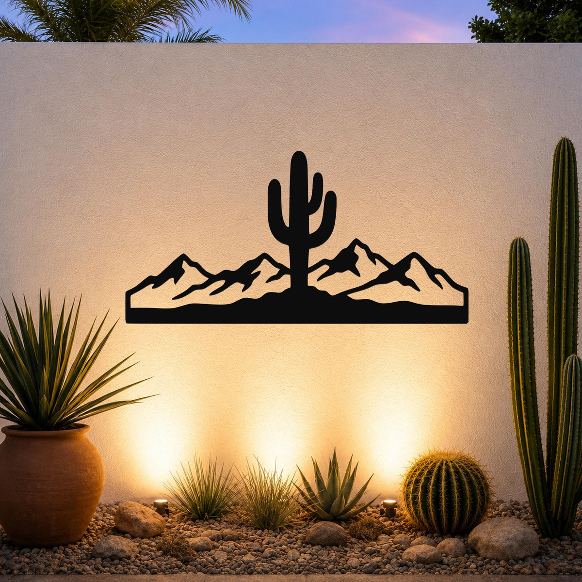 Black metal wall art silhouette of a saguaro cactus and mountain range, mounted on an outdoor wall above a desert garden with potted plants and ground lights.