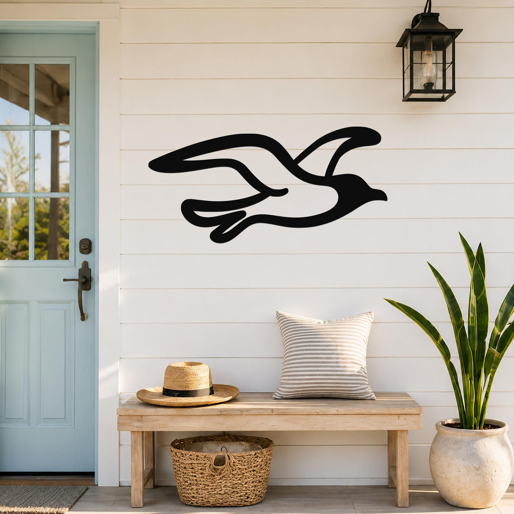 Black metal seagull wall art with flowing wing cutouts, mounted on a white shiplap wall above a wooden bench in a coastal entryway.