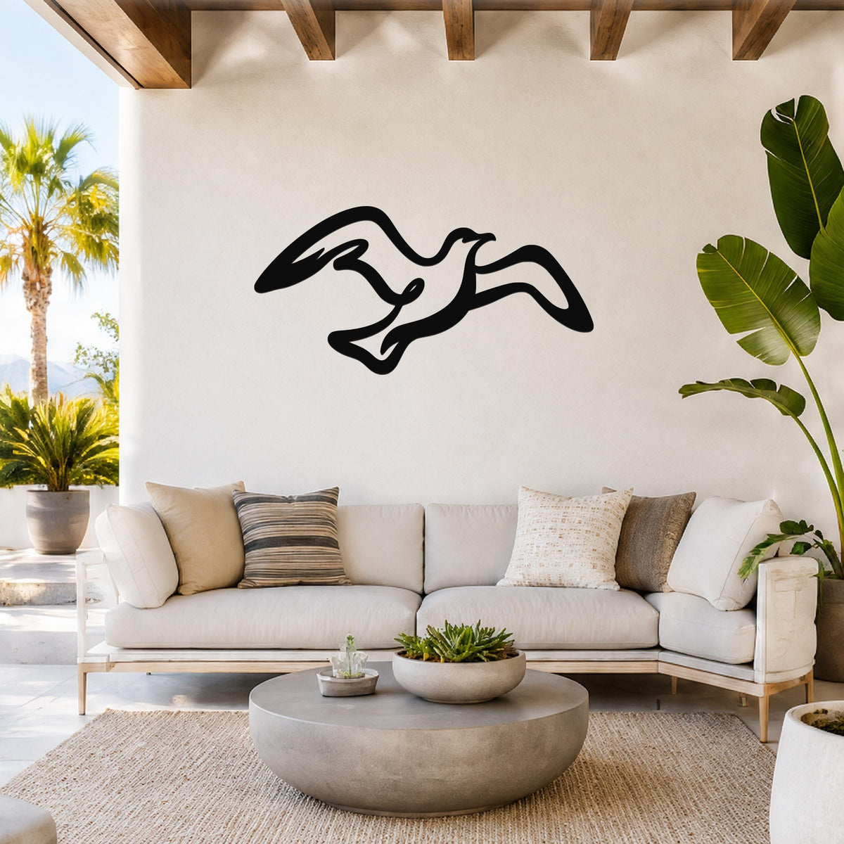 Black metal seagull wall art with flowing silhouette cutout, mounted above a white sofa in a coastal living room.