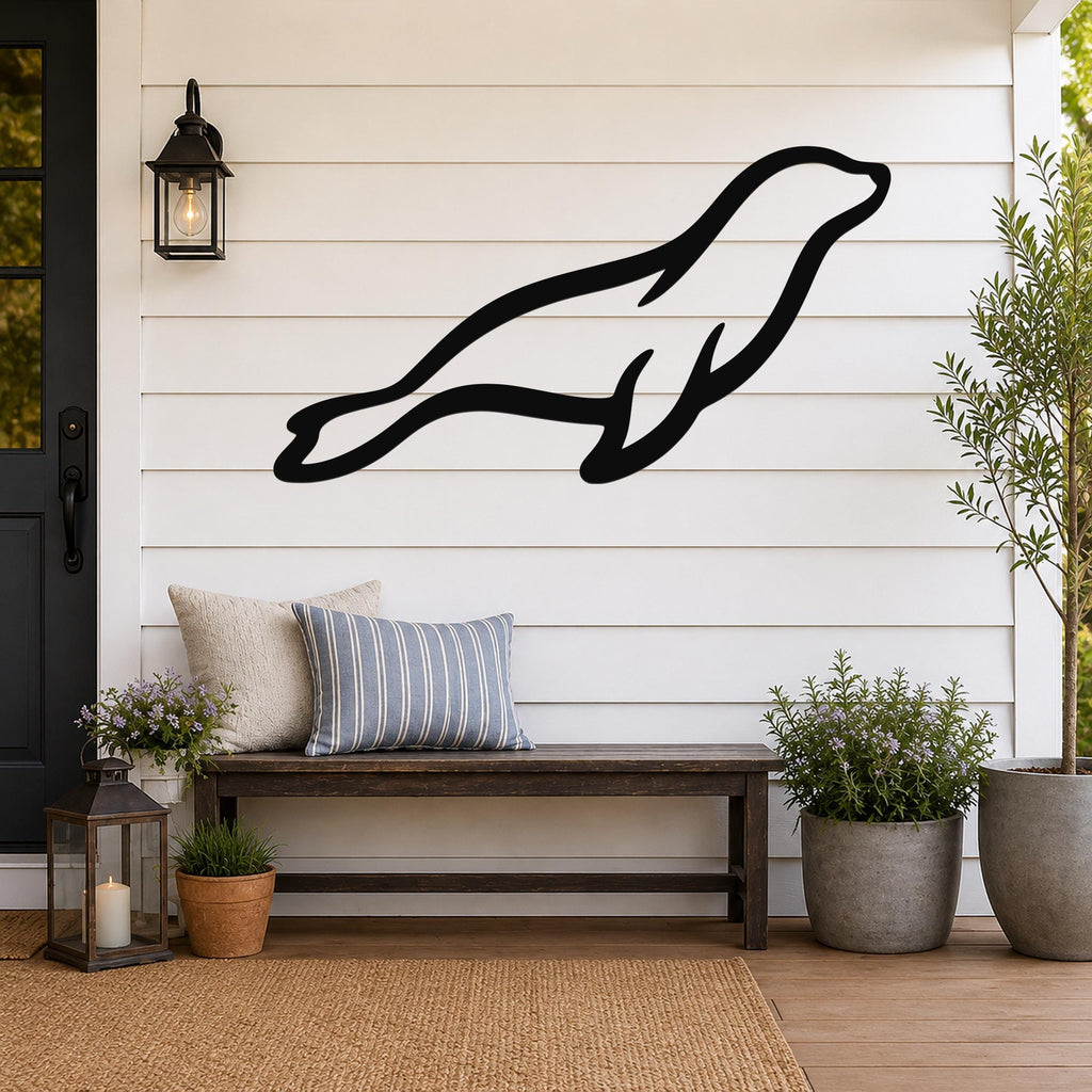 Black metal sea lion wall art silhouette mounted on a white shiplap wall above a wooden bench on a porch.