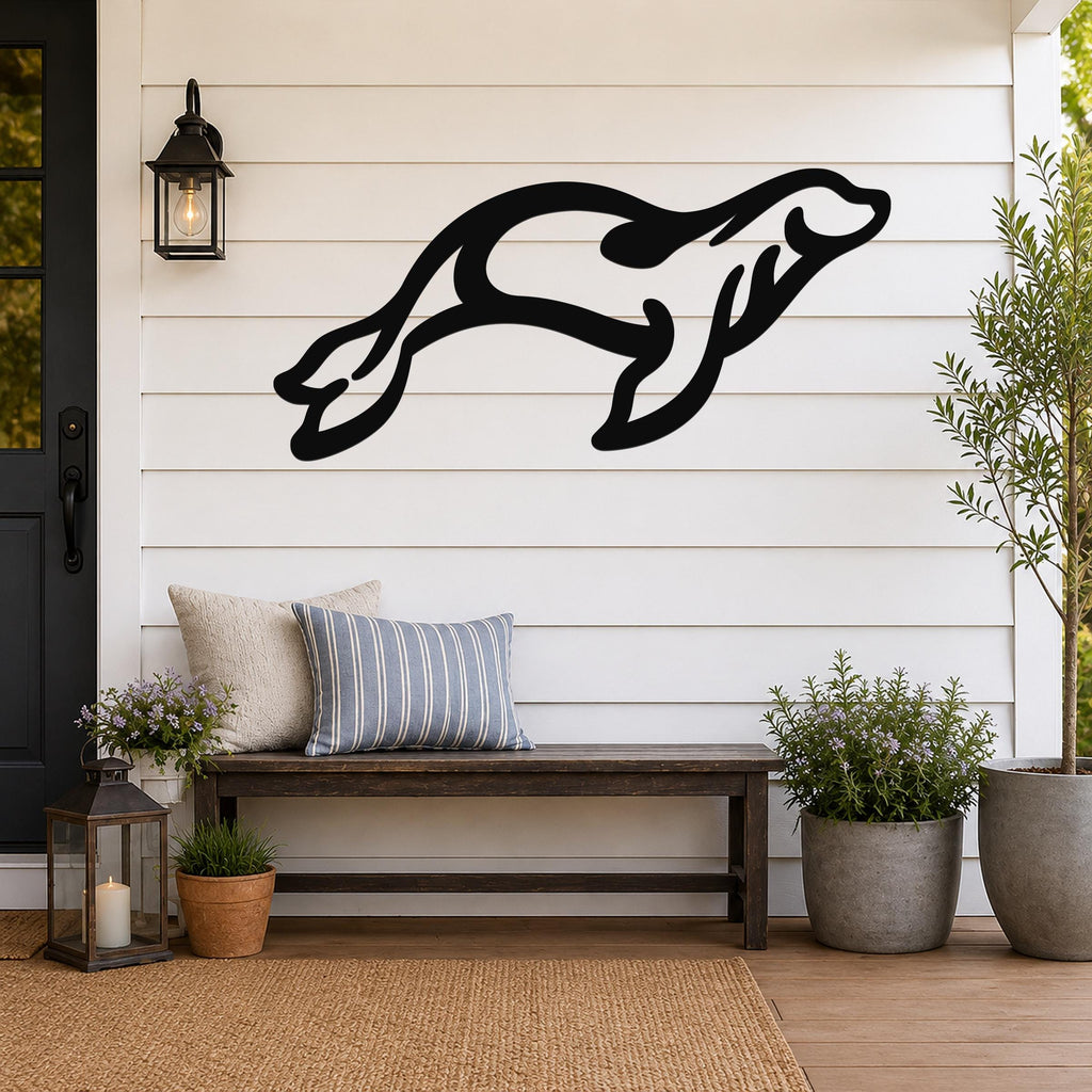 Black metal sea lion wall art in a dynamic leaping silhouette, mounted on a white shiplap wall above a wooden bench on a porch.