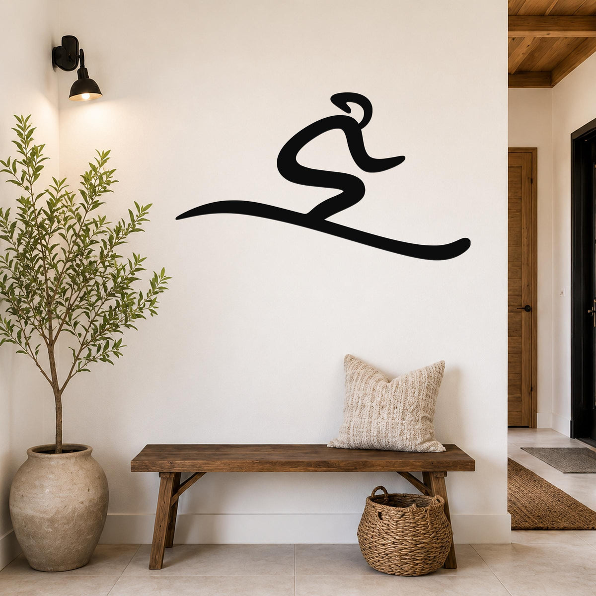 Black metal wall art in a flowing, abstract skiing silhouette, mounted on a white wall above a wooden bench in a modern entryway.