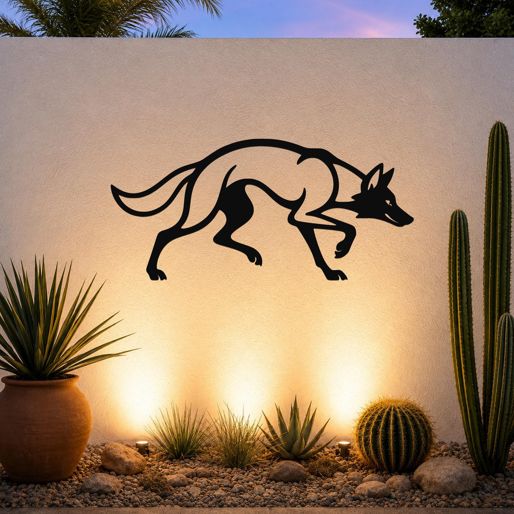 Black metal coyote wall art silhouette with motion-line cutouts, mounted on an outdoor wall above a desert garden with cacti and warm uplighting.