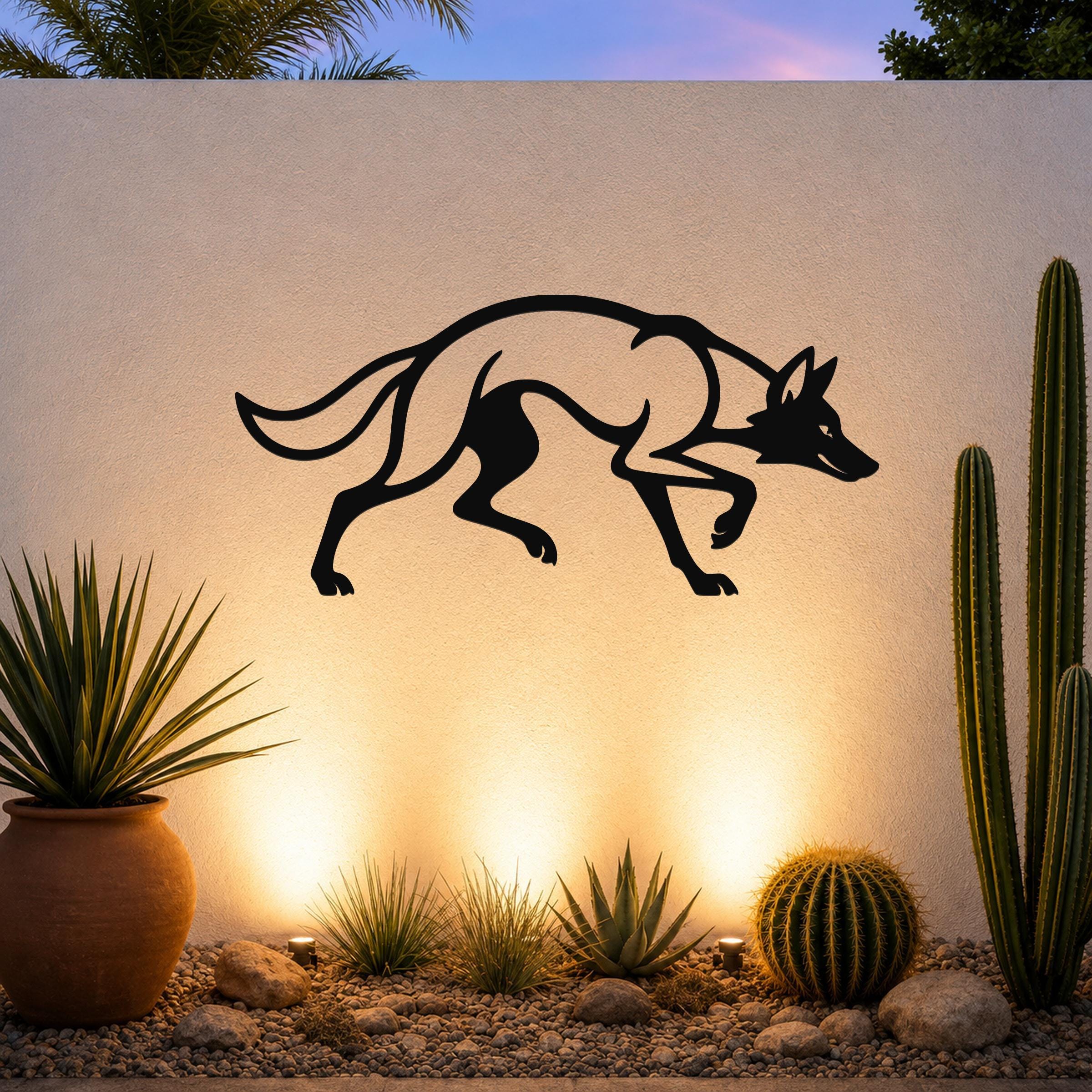 Black metal coyote wall art silhouette with motion-line cutouts, mounted on an outdoor wall above a desert garden with cacti and warm uplighting.