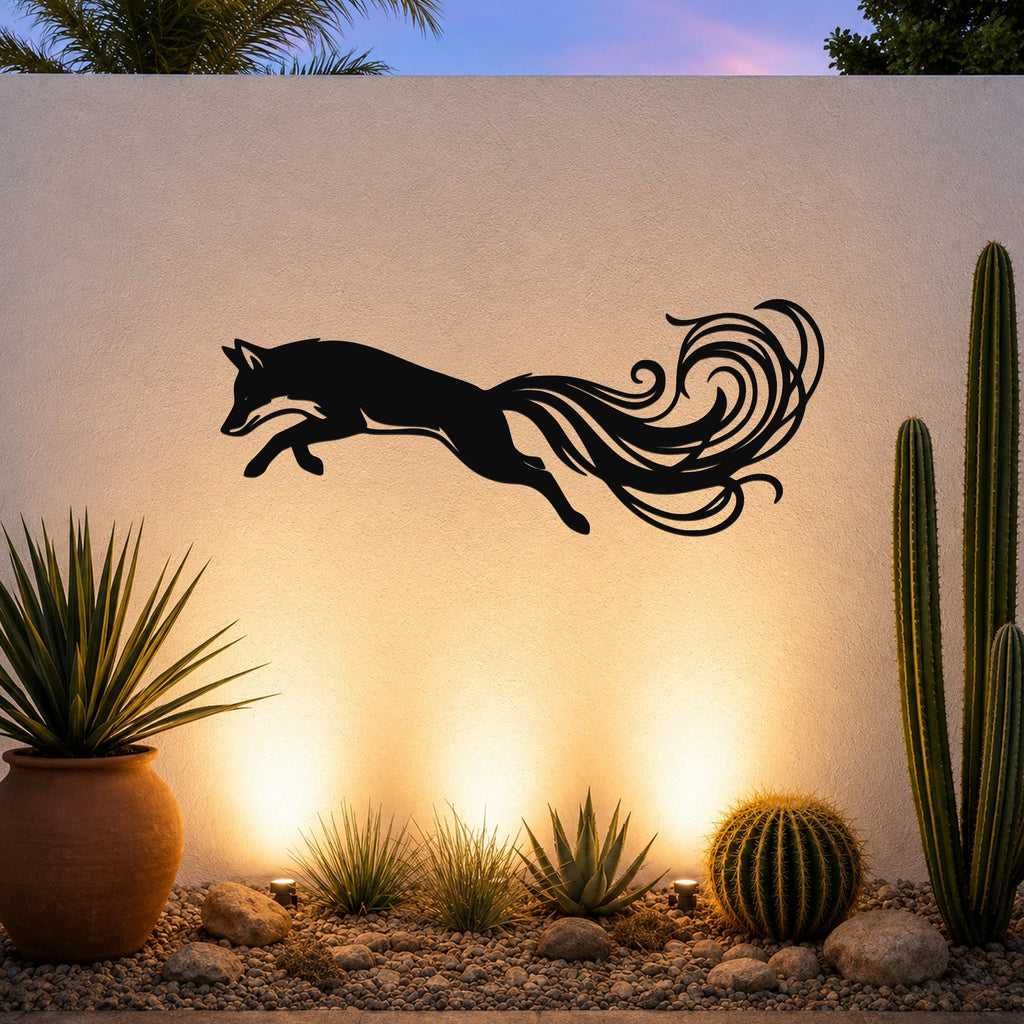 Black metal fox wall art with flowing tail cutouts, mounted on an outdoor wall above a desert garden with cacti and warm uplighting.