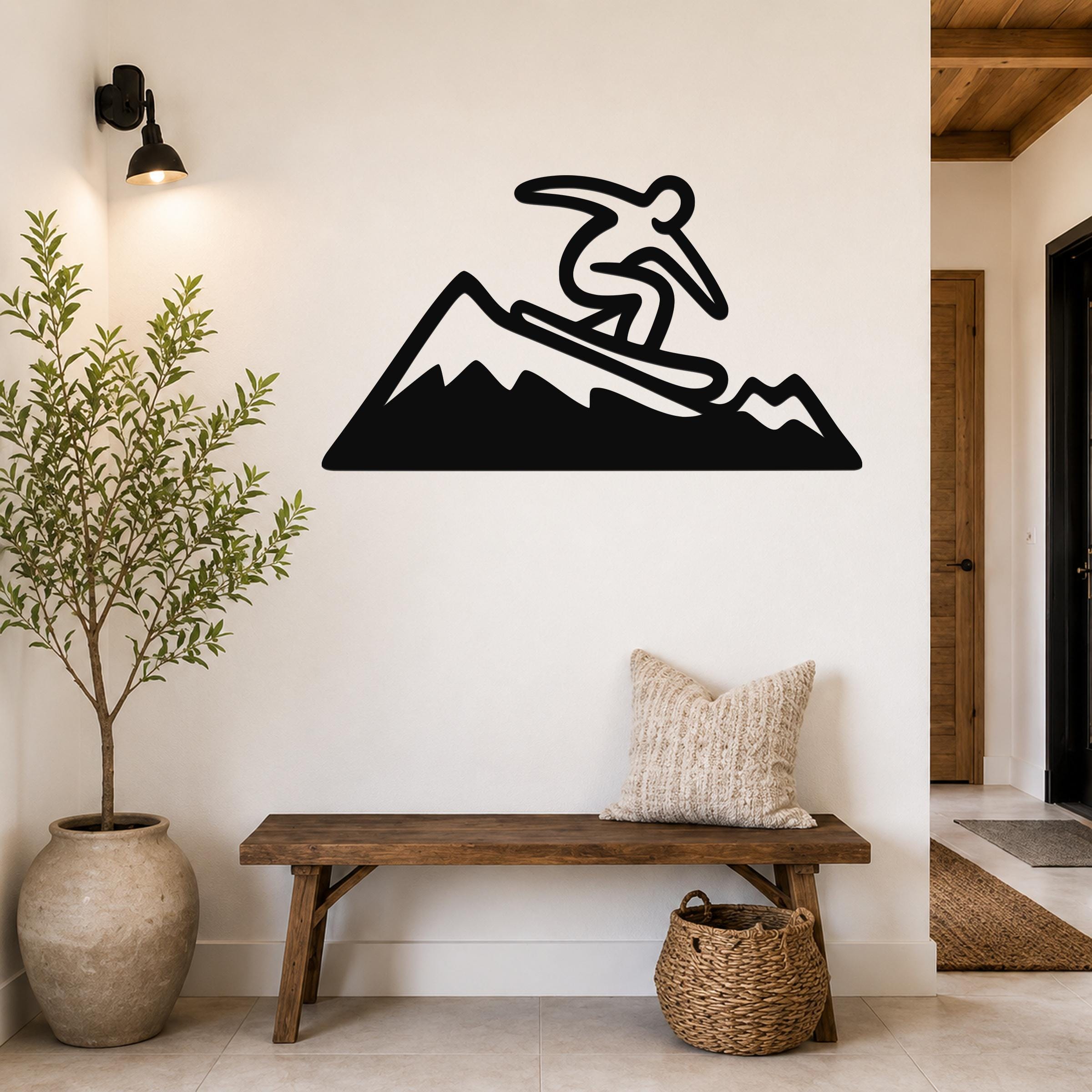 Black metal wall art silhouette of a snowboarder on a mountain, mounted above a wooden bench in a hallway.
