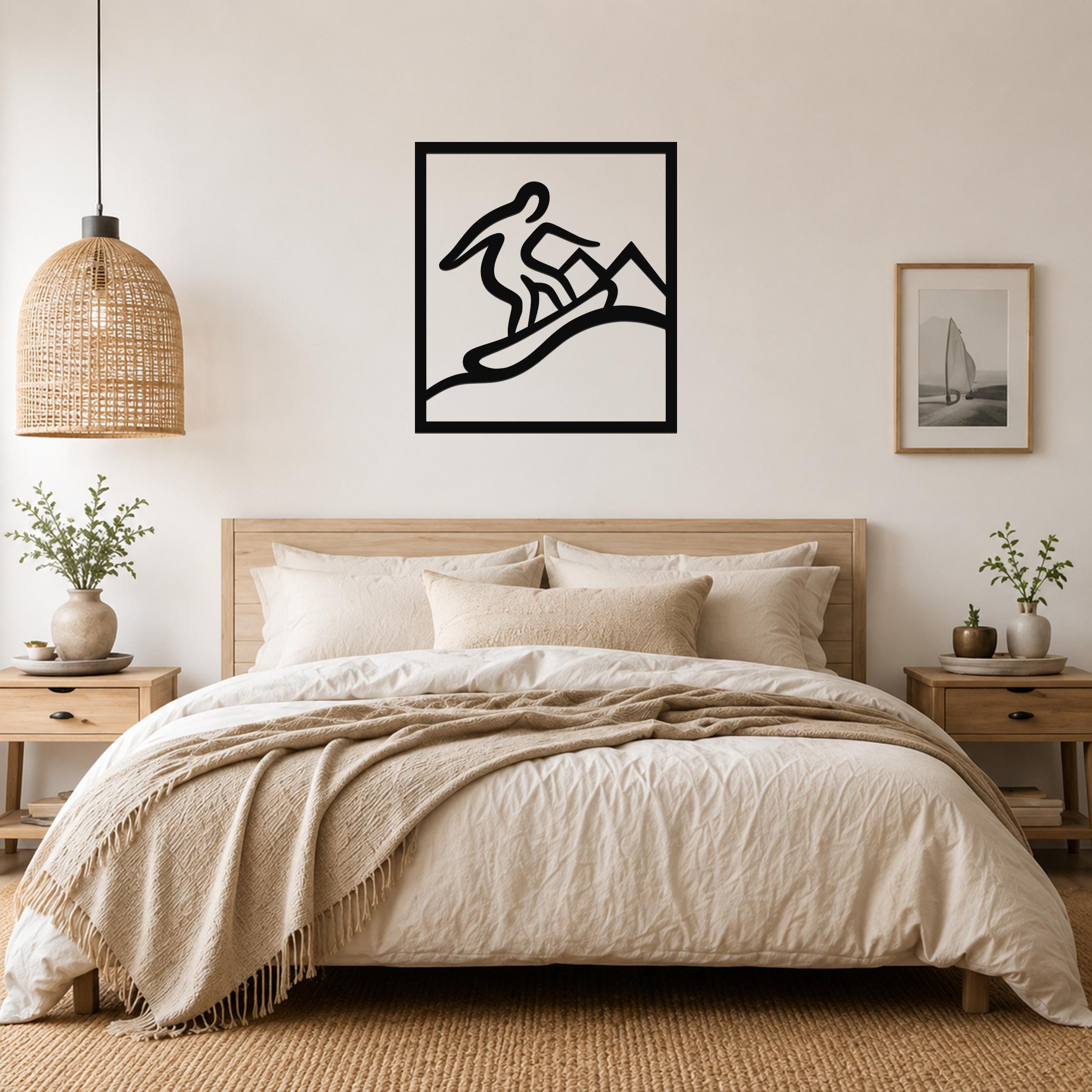 Black metal wall art with a snowboarder silhouette in motion, mounted above a bed in a neutral bedroom.