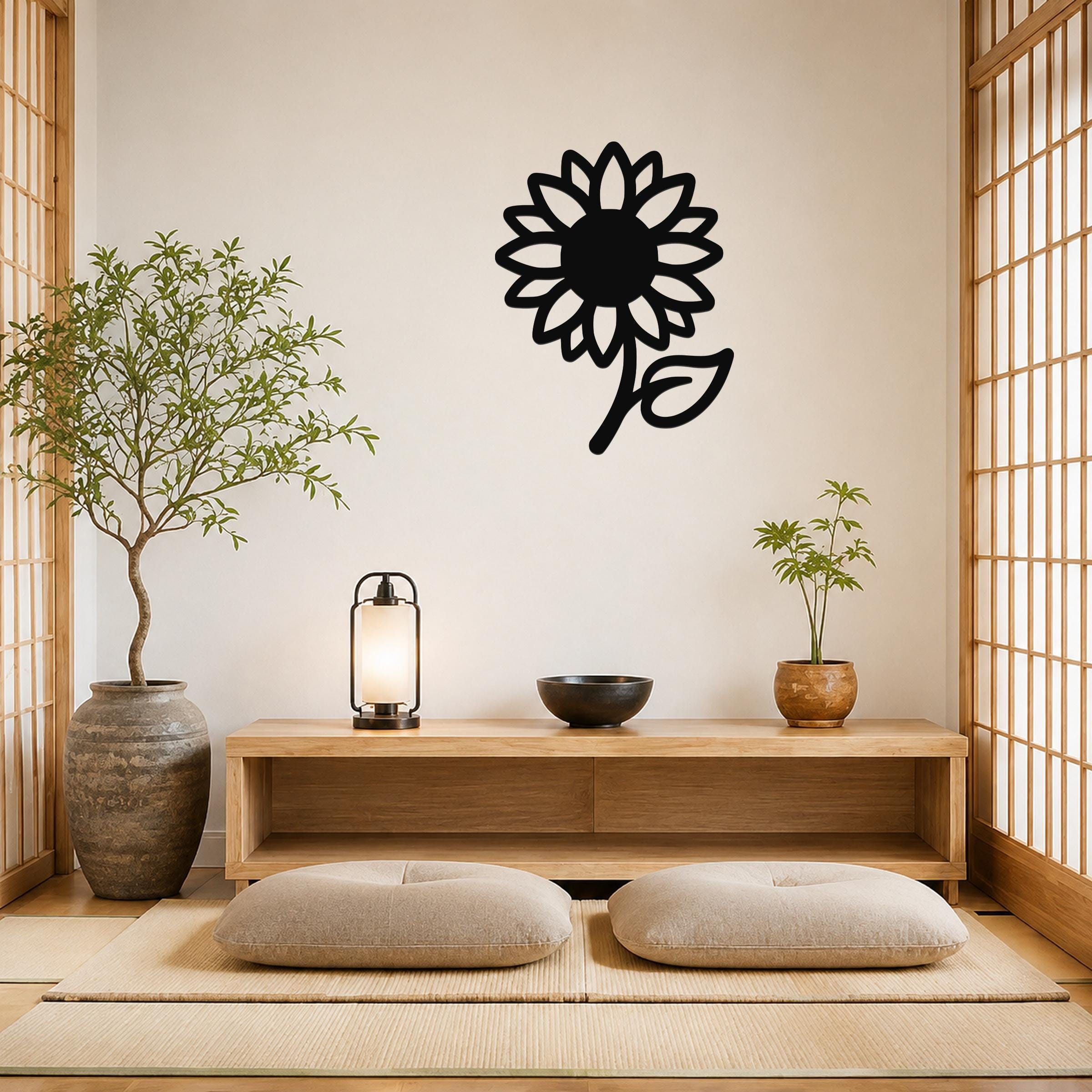 Black metal sunflower wall art with a bold silhouette and leaf detail, mounted on a wall above a wooden console in a minimalist room.