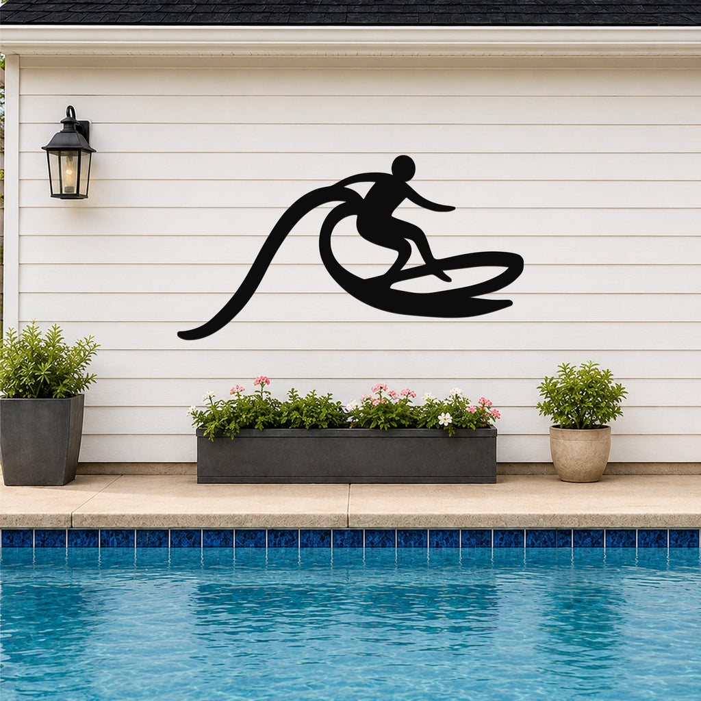 Black metal surfer wall art with wave motion cutout, mounted on a white siding wall above a poolside planter.