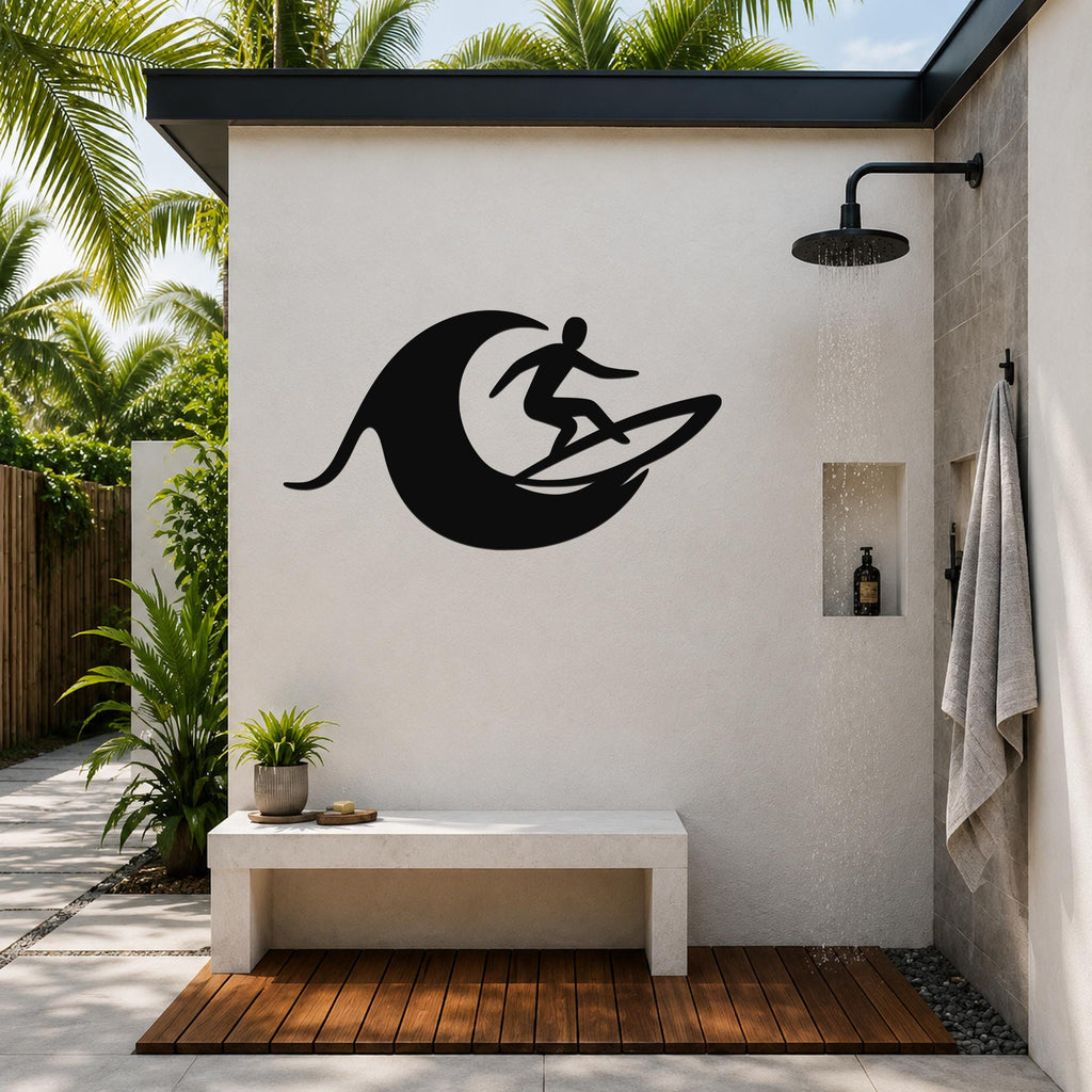 Black metal surfer wall art with wave cutout, mounted on an outdoor shower wall above a bench in a tropical patio setting.