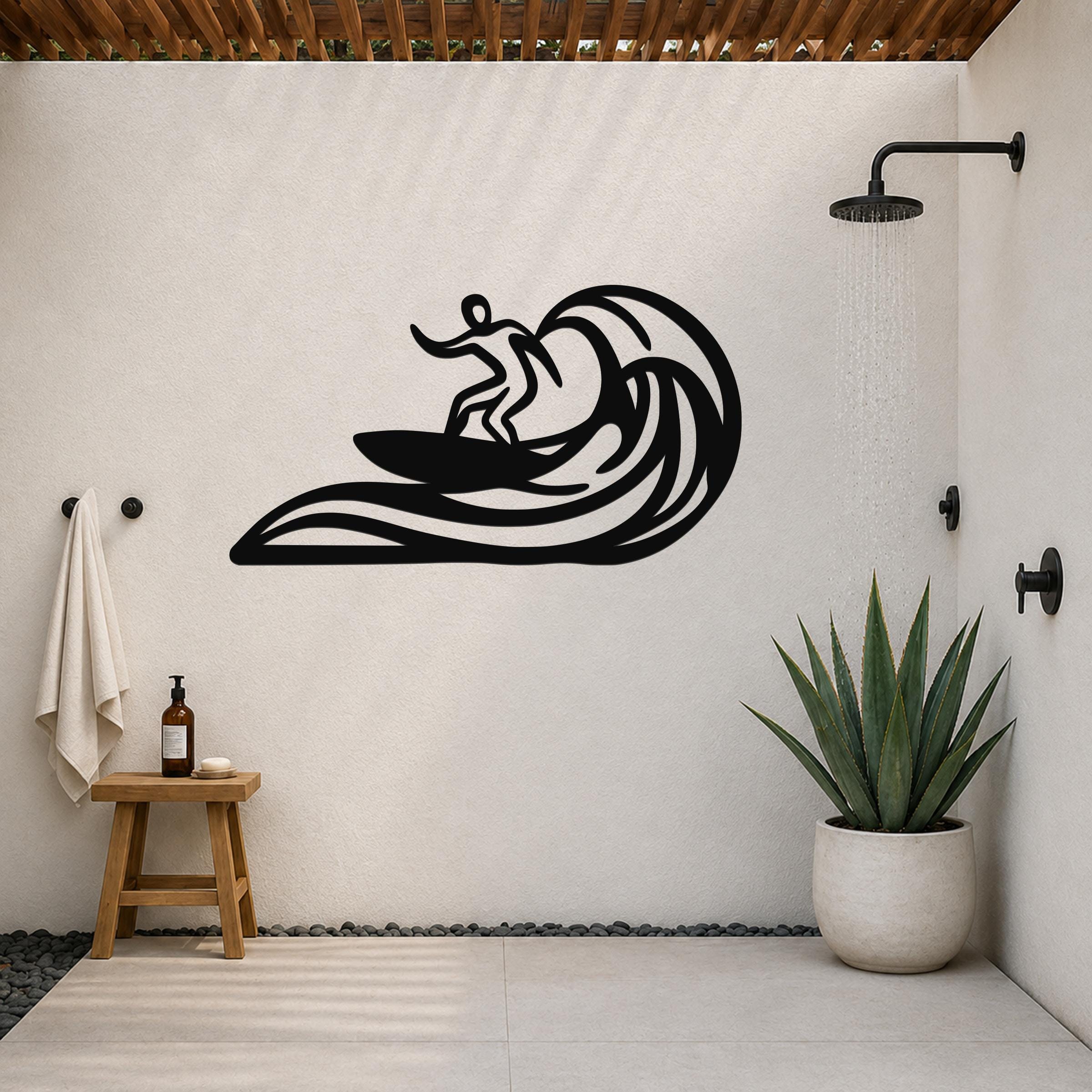 Black metal surfer wall art with wave cutouts, mounted on a white outdoor shower wall above a small wooden stool and potted plant.