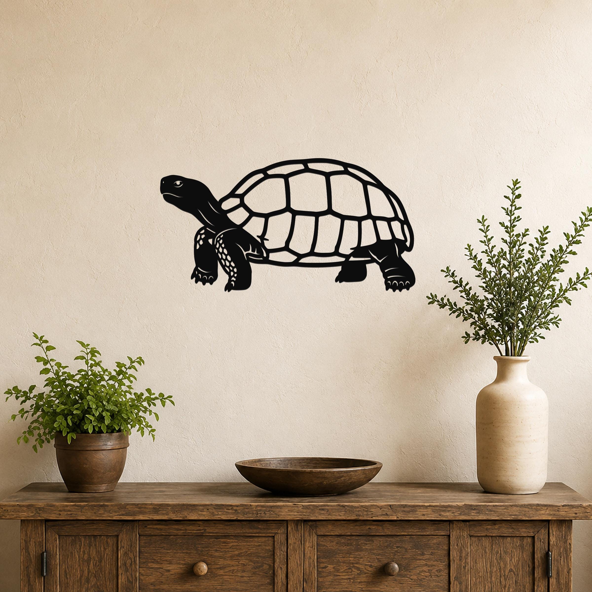 Black metal tortoise wall art with detailed shell and limb cutouts, mounted on a beige wall above a wooden console table with plants.