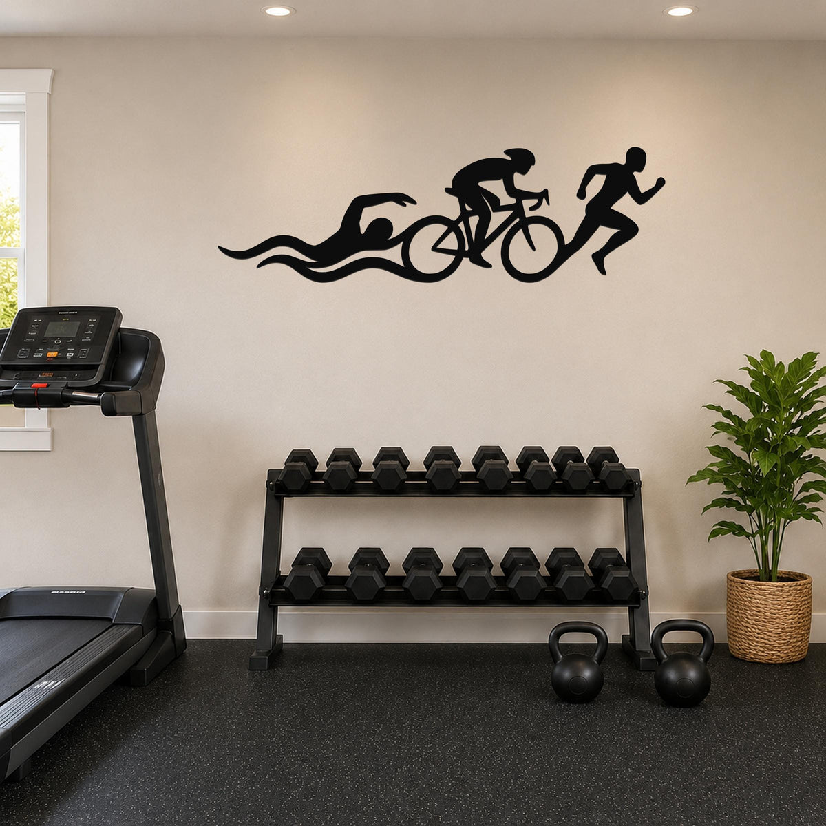 Black metal triathlon wall art with swim, bike, and run silhouettes and motion lines, mounted on a wall above a dumbbell rack in a home gym.