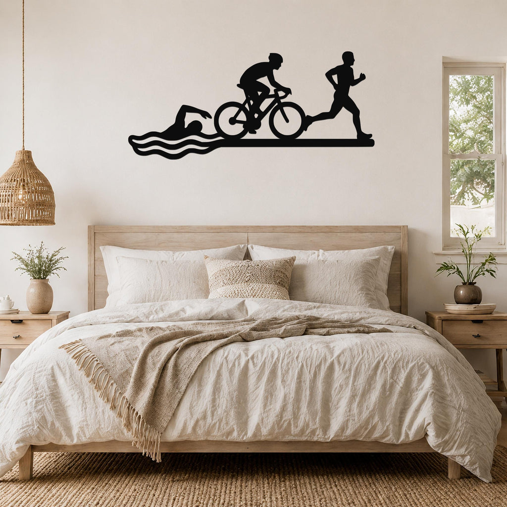 Black metal wall art silhouette of a triathlon scene—swimmer, cyclist, and runner—mounted above a bed in a bedroom.