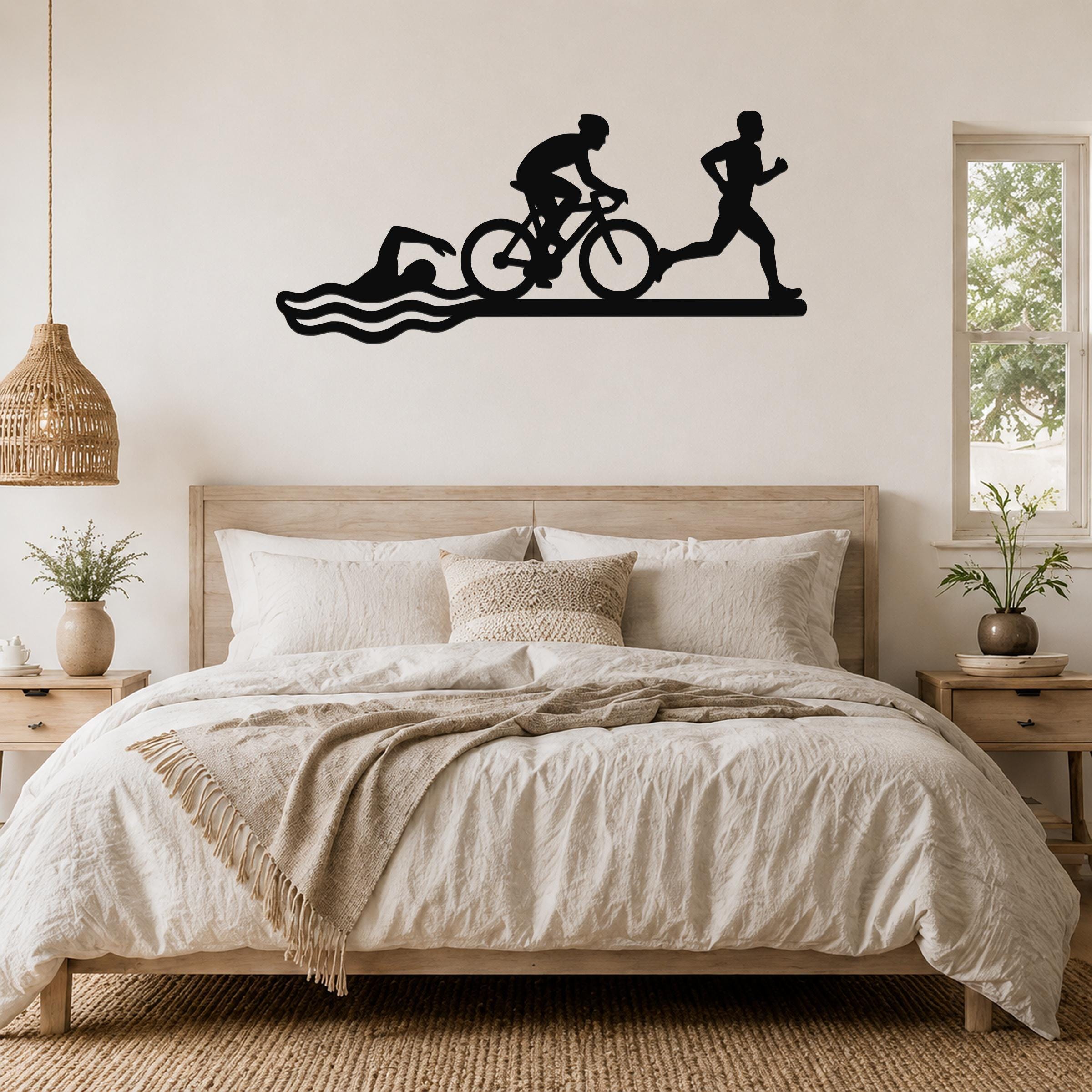 Black metal wall art silhouette of a triathlon scene—swimmer, cyclist, and runner—mounted above a bed in a bedroom.