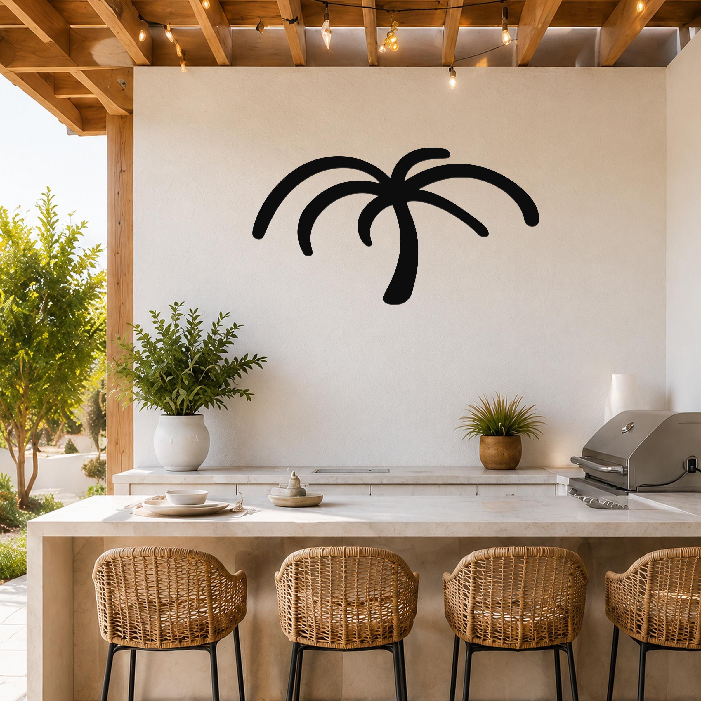 Black metal palm tree wall art with curved frond cutouts, mounted on a white wall above a kitchen counter in a covered outdoor patio.