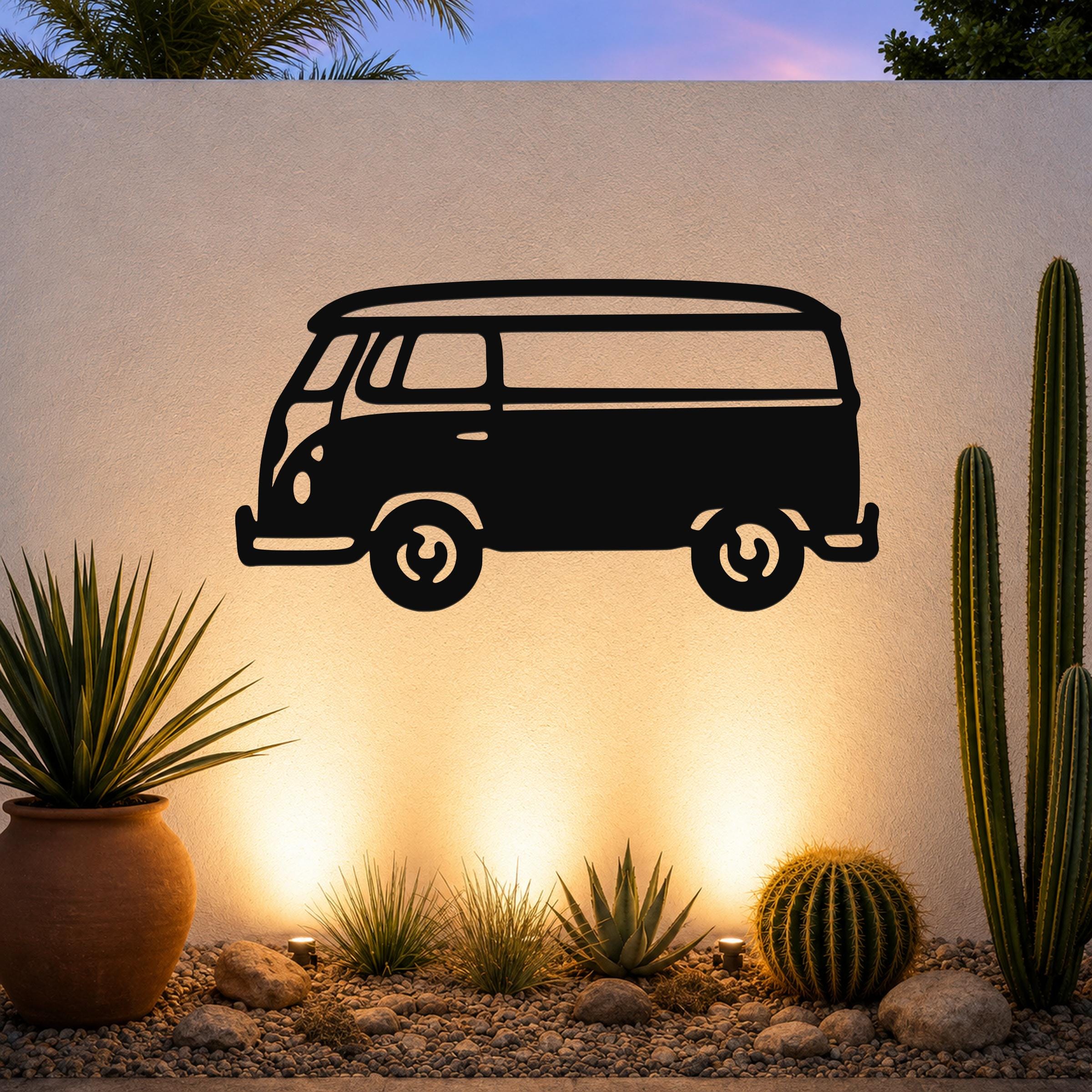 Black metal vintage van wall art silhouette with cutout wheels and windows, mounted on an outdoor wall above a desert garden with cacti and warm uplighting.