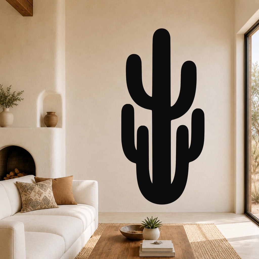 Black metal saguaro cactus wall art with branch cutouts, mounted on a living room wall above a white sofa.