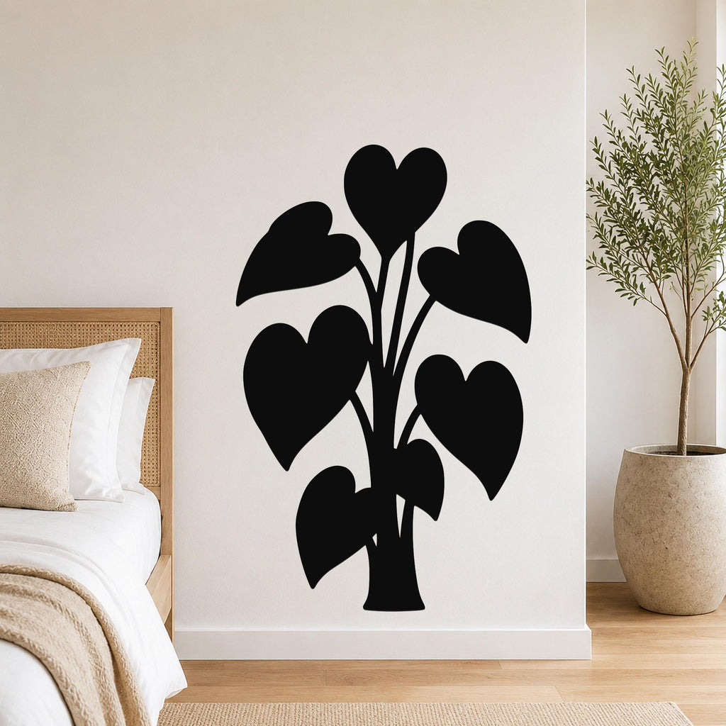 Black metal wall art in the silhouette of a philodendron with heart-shaped leaves, mounted on a white wall above a bed in a bedroom.