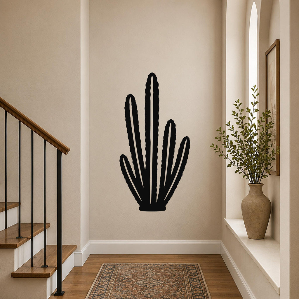 Black metal cactus wall art with multiple vertical arms and internal cutouts, mounted on a hallway wall above a patterned rug near a staircase.