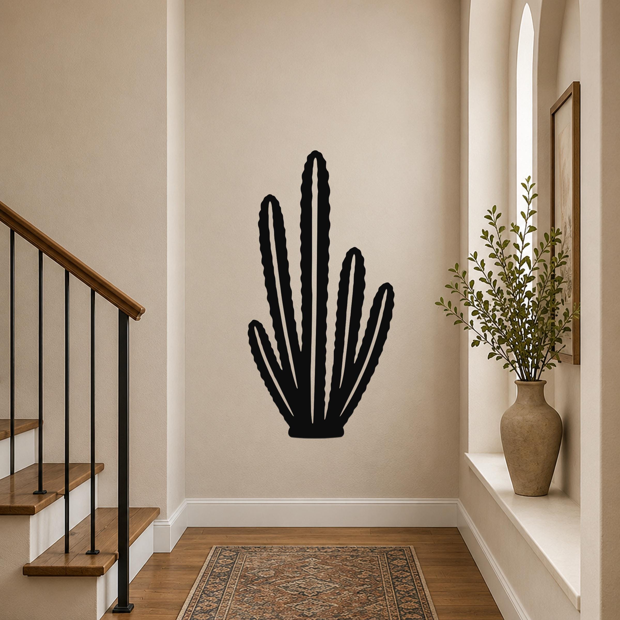 Black metal cactus wall art with multiple vertical arms and internal cutouts, mounted on a hallway wall above a patterned rug near a staircase.