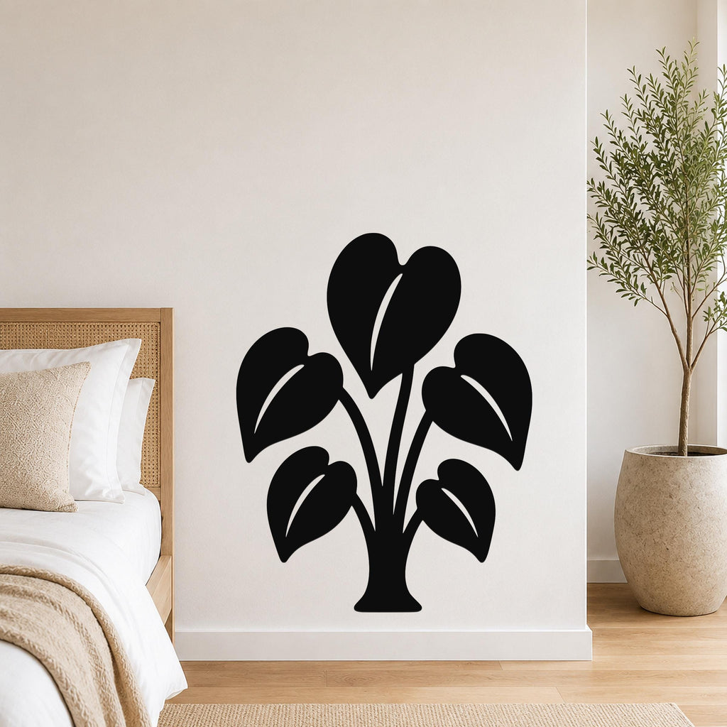 Black metal wall art in the shape of an elephant ear plant with leaf cutouts, mounted on a bedroom wall above a bed.