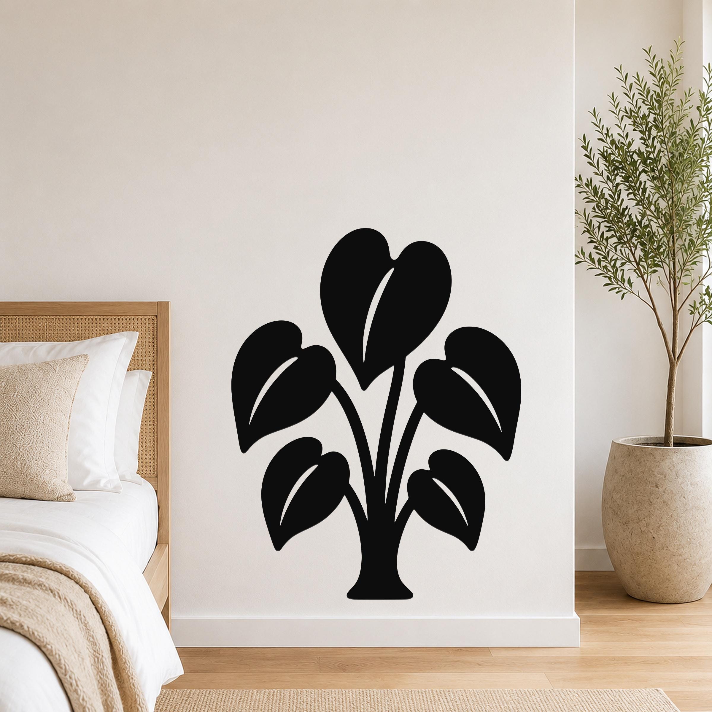 Black metal wall art in the shape of an elephant ear plant with leaf cutouts, mounted on a bedroom wall above a bed.