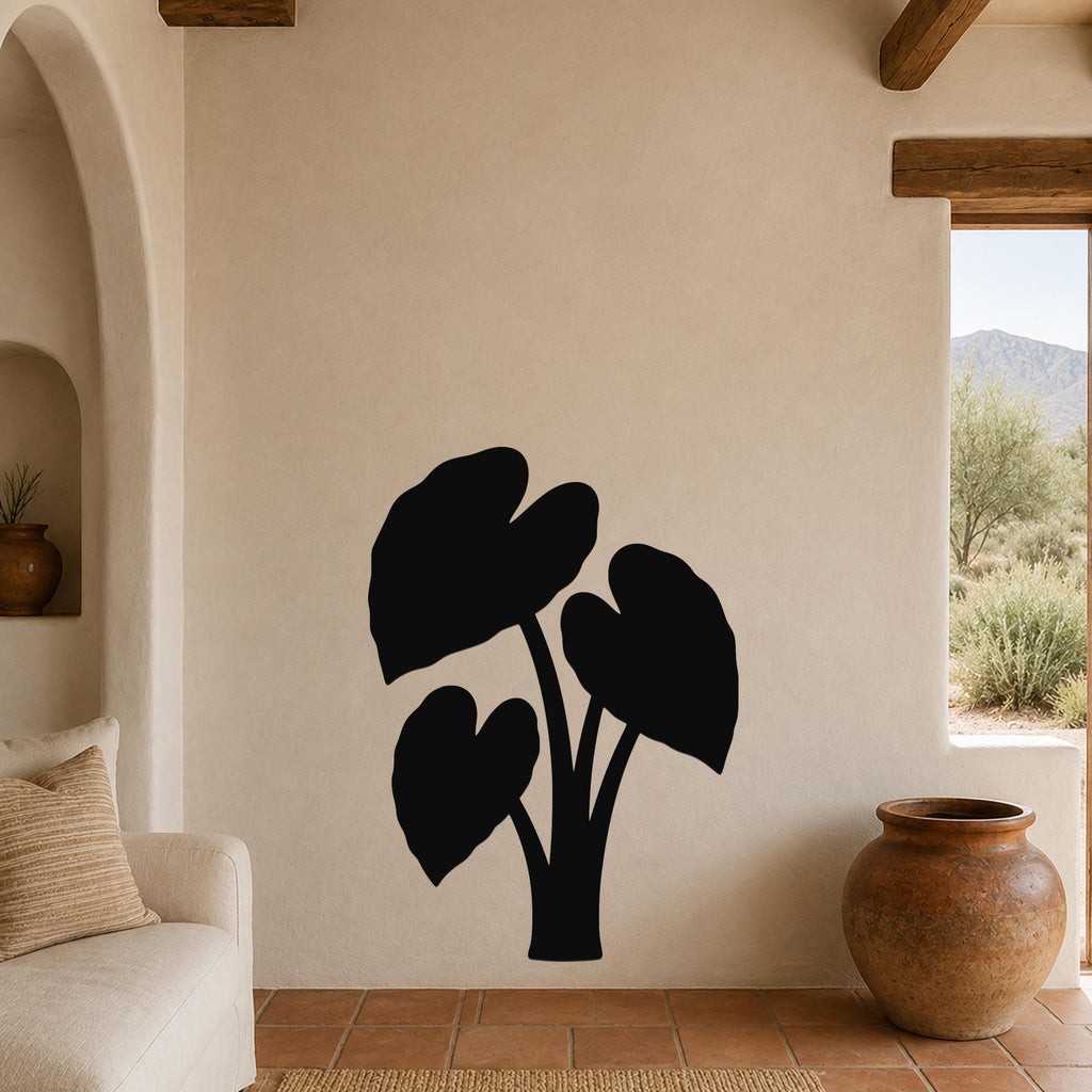 Black metal wall art in the silhouette of an elephant ear plant, mounted on a beige living room wall above a sofa.