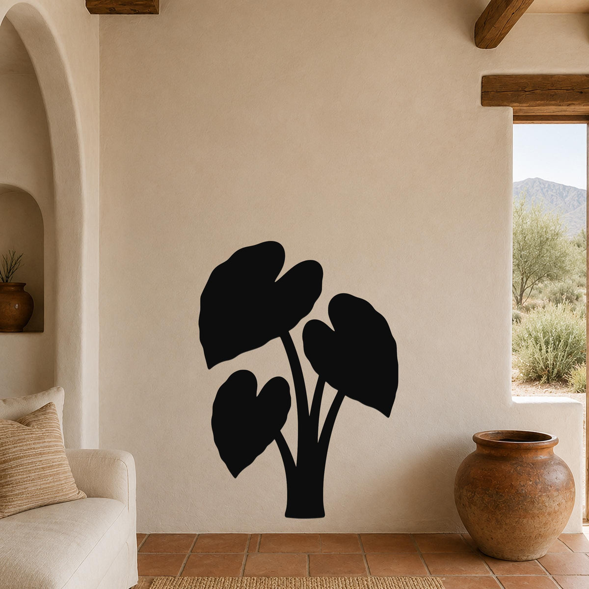 Black metal wall art in the silhouette of an elephant ear plant, mounted on a beige living room wall above a sofa.