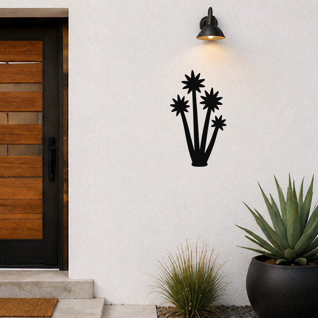 Black metal yucca wall art with star-shaped bloom cutouts, mounted on a white exterior wall beside a front door and potted plants.