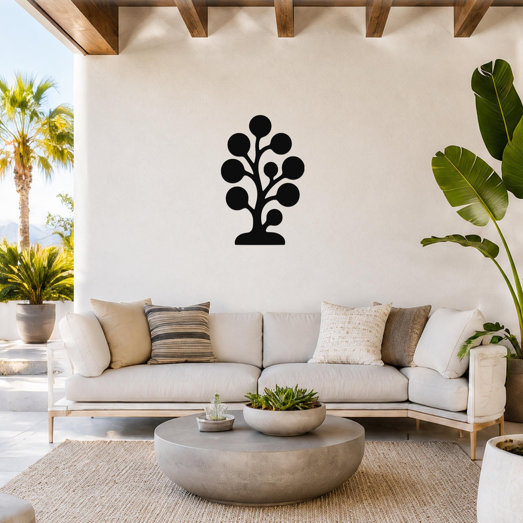 Black metal wall art in a stylized tree silhouette with circular leaf shapes, mounted on a white wall above a light-colored sofa in a bright living room.