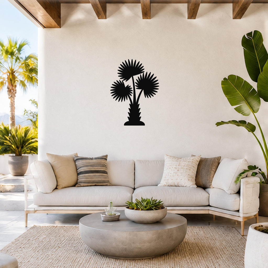 Black metal palm tree wall art with three fan-shaped fronds, mounted on a white wall above a light-colored sofa in a bright living room.