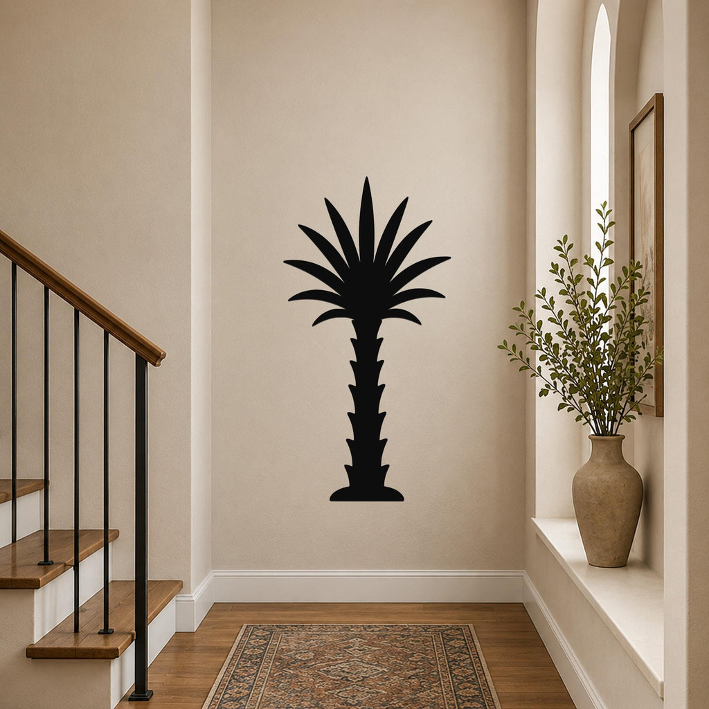 Black metal palm tree wall art silhouette mounted on a hallway wall above a patterned rug, near a staircase and a vase with greenery.