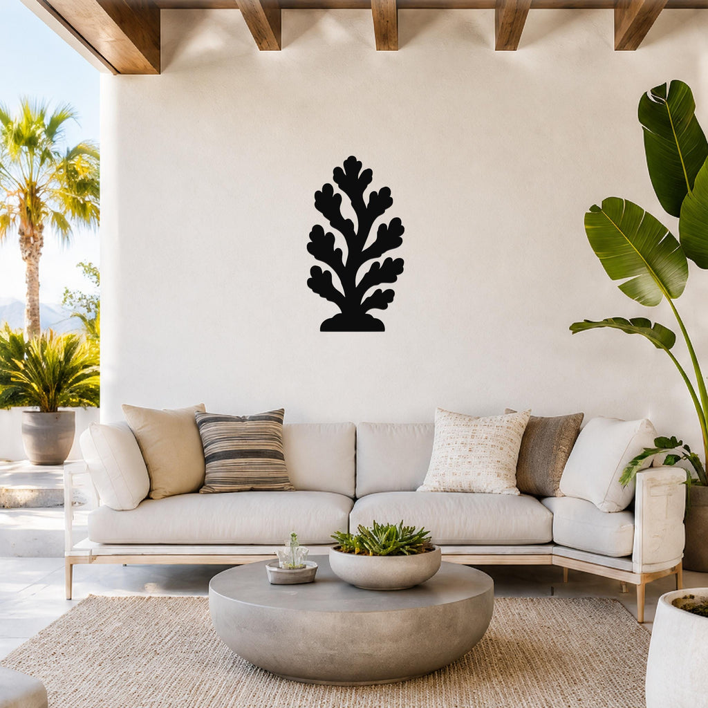 Black metal coral wall art with branching cutouts, mounted on a white wall above a light-colored sofa in a bright outdoor living space.