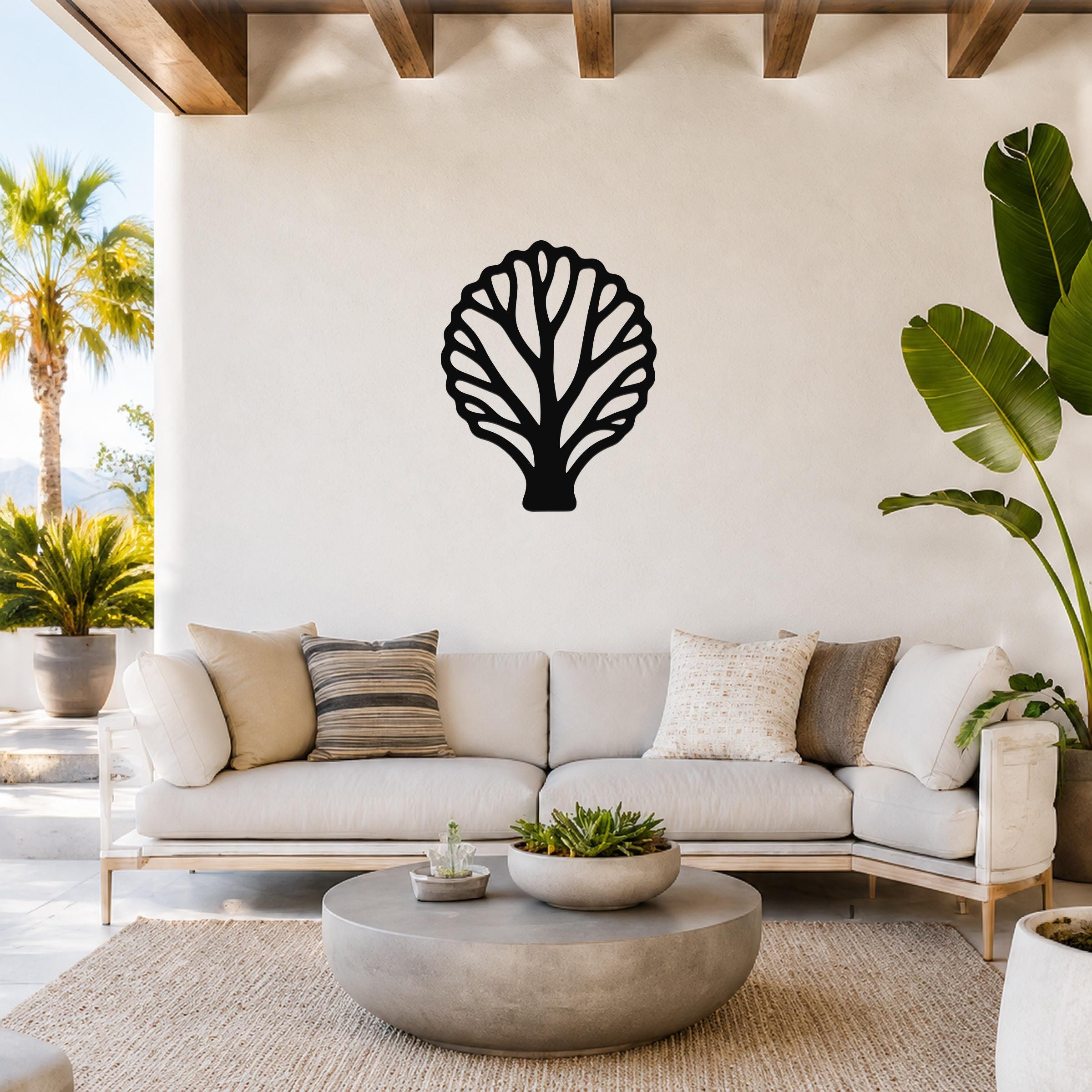 Black metal fan coral wall art with intricate cutout branches, mounted on a white wall above a light-colored sofa in a bright outdoor living space.
