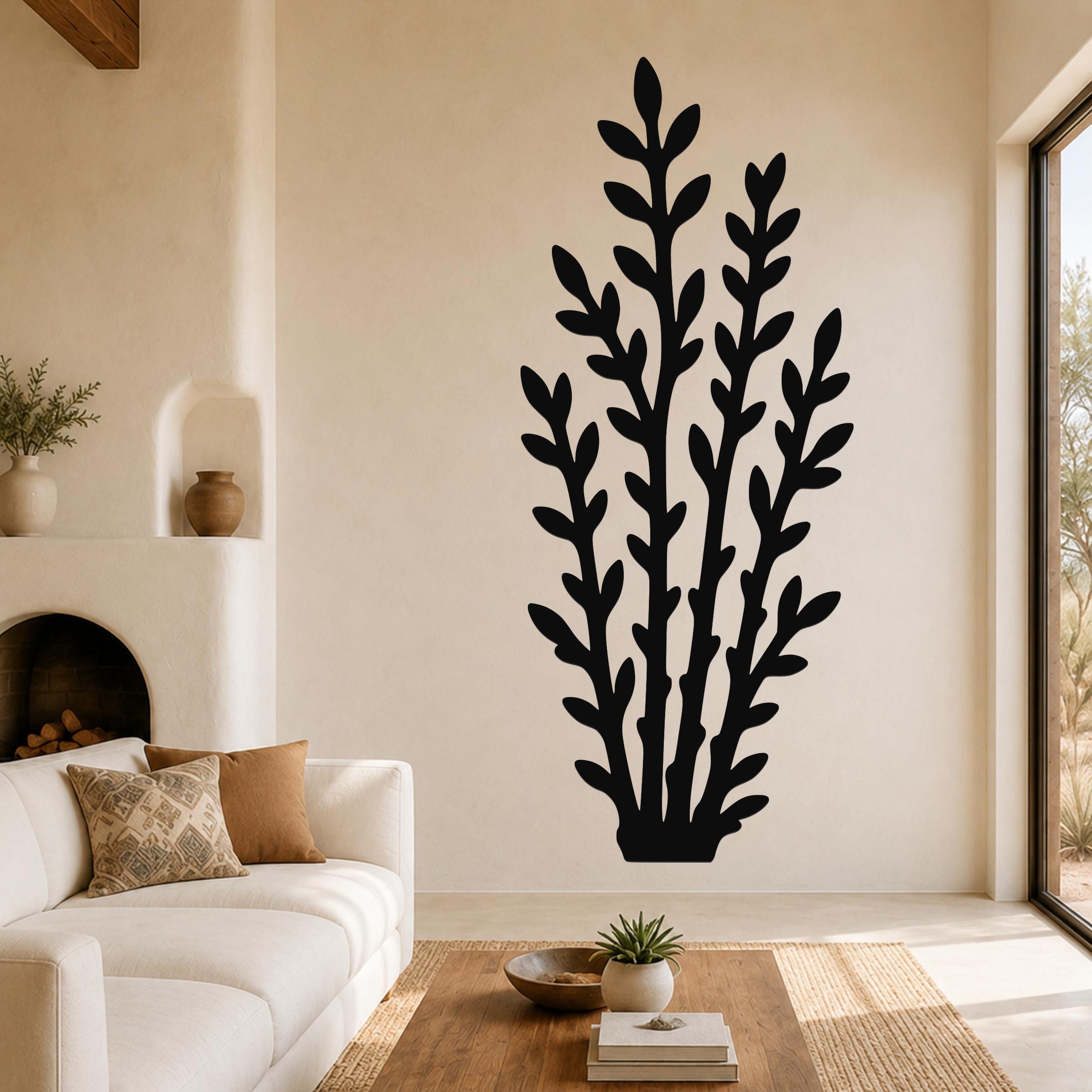 Black metal wall art with a leafy branch silhouette, mounted on a living room wall above a white sofa.