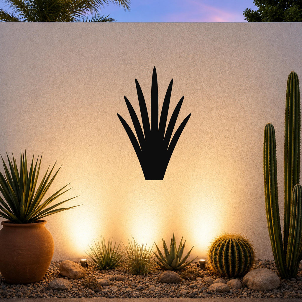 Black metal yucca wall art silhouette mounted on a textured outdoor wall above a desert garden with cacti and warm uplighting.