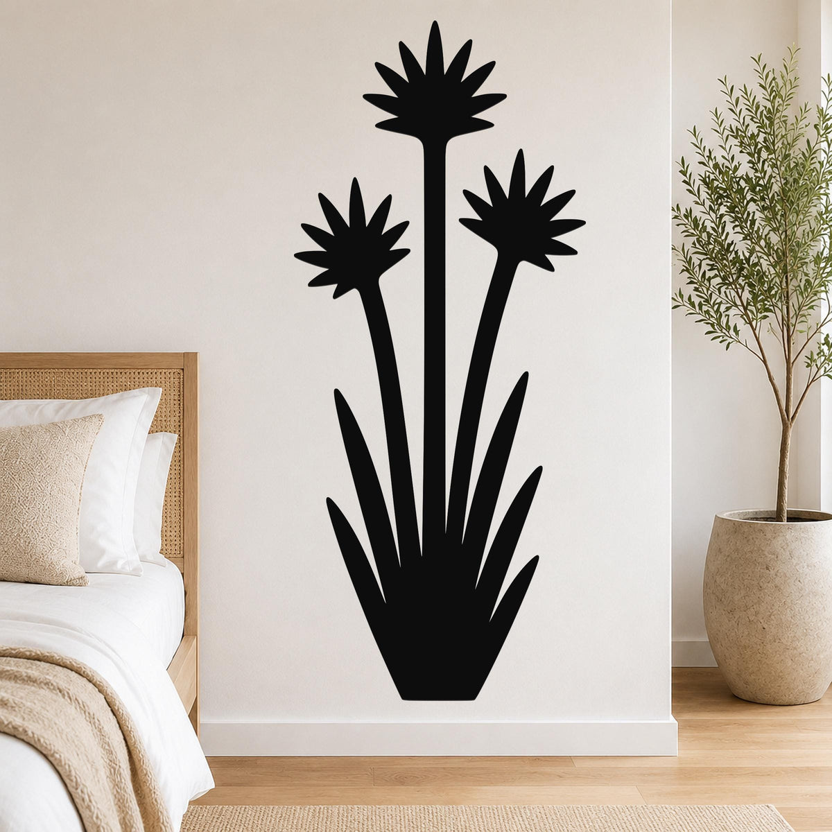 Black metal wall art in a yucca plant silhouette with three starburst flowers and long leaves, mounted on a bedroom wall above a bed.