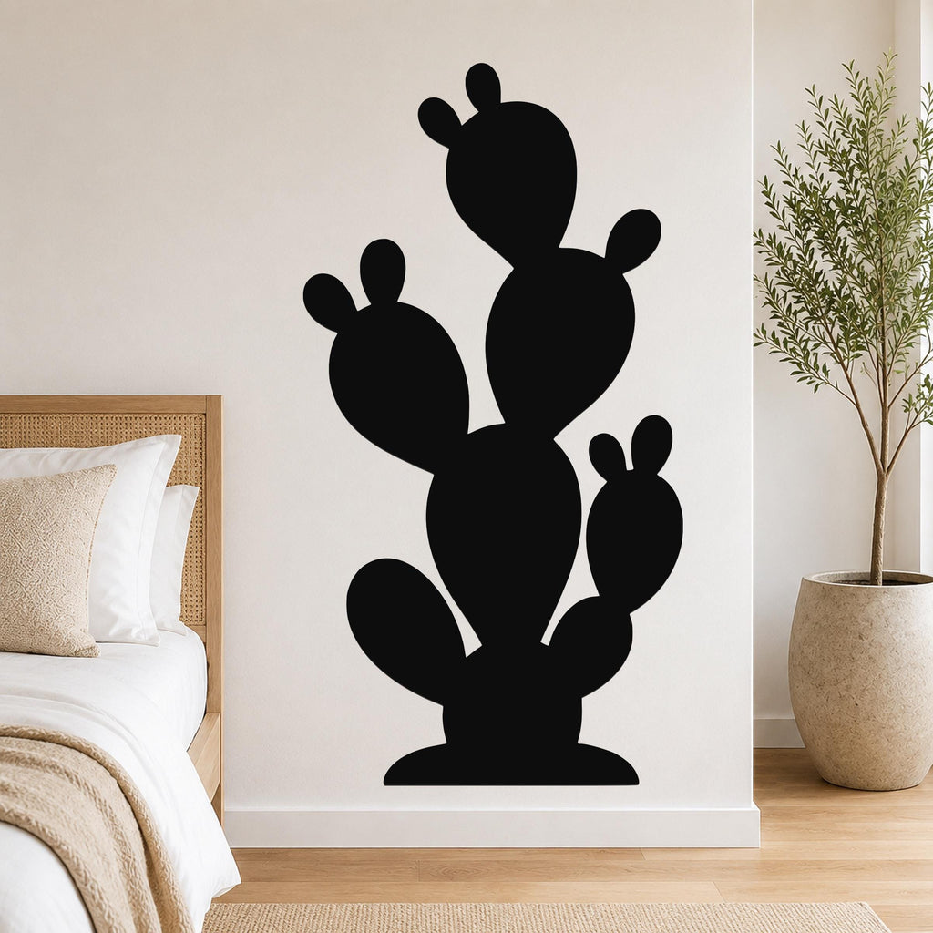 Black metal cactus wall art with multiple rounded segments and cutout details, mounted on a white bedroom wall above a bed.