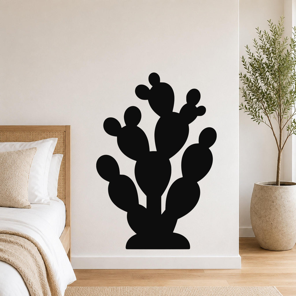Black metal prickly pear cactus wall art with multiple rounded pads and cutout details, mounted on a white bedroom wall above a bed.