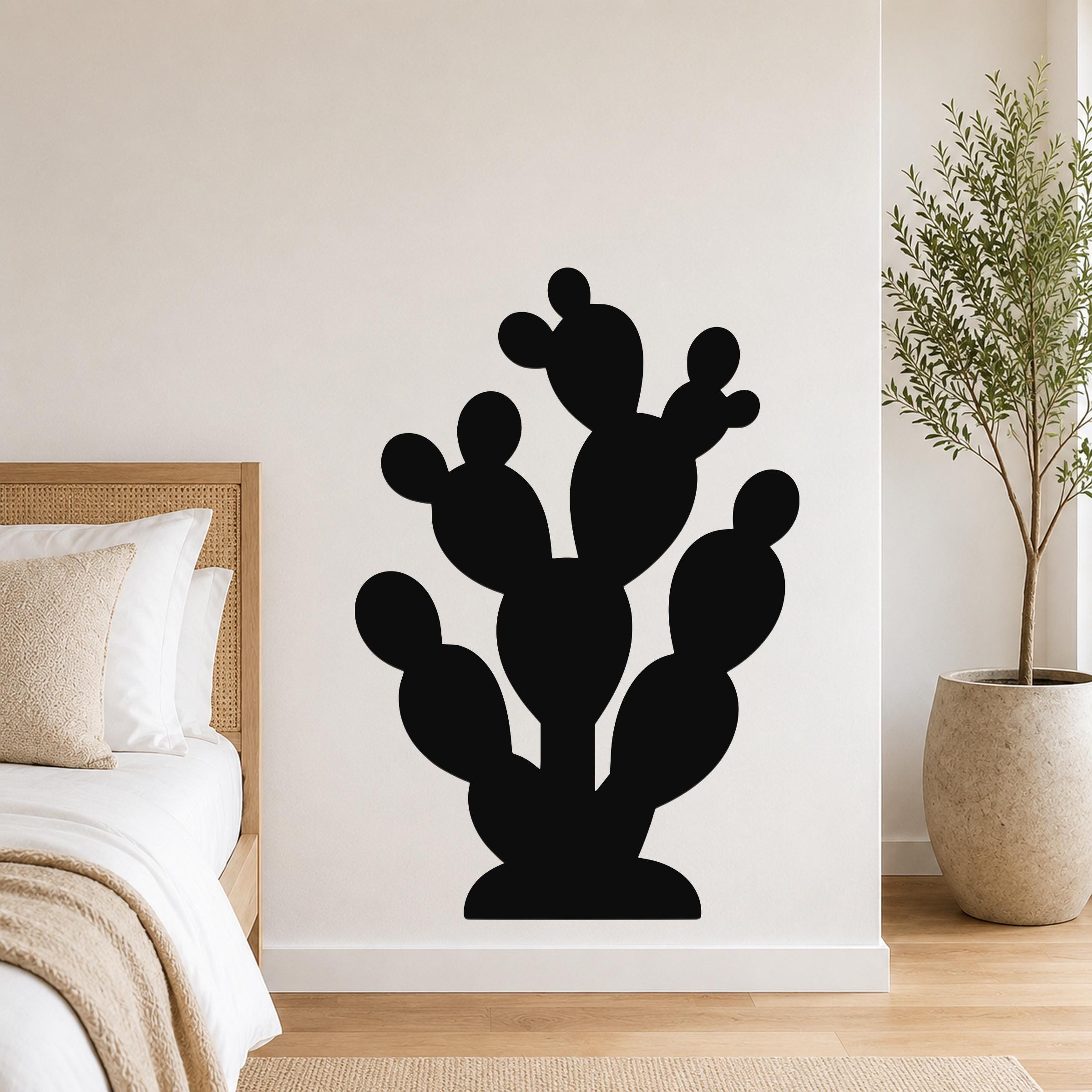 Black metal prickly pear cactus wall art with multiple rounded pads and cutout details, mounted on a white bedroom wall above a bed.