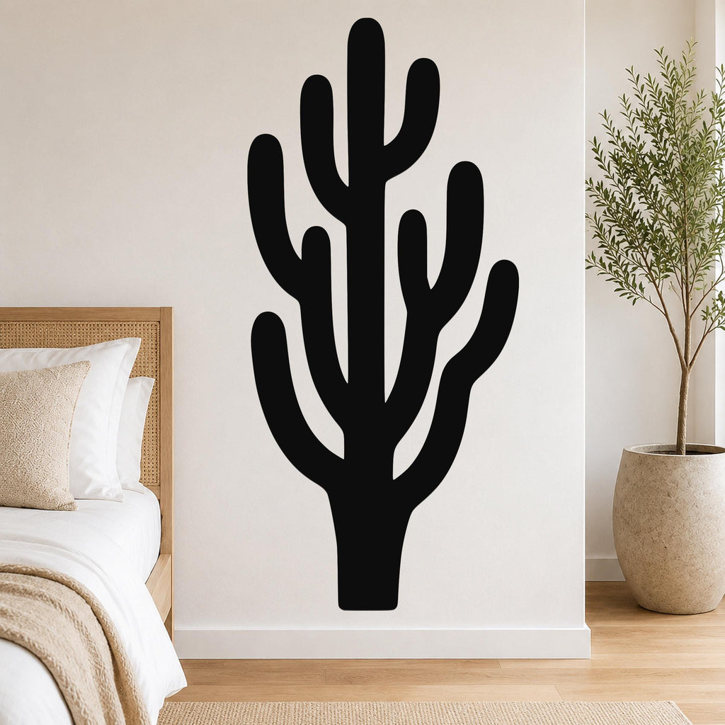 Black metal saguaro cactus wall art with branching cutouts, mounted on a white bedroom wall above a bed.