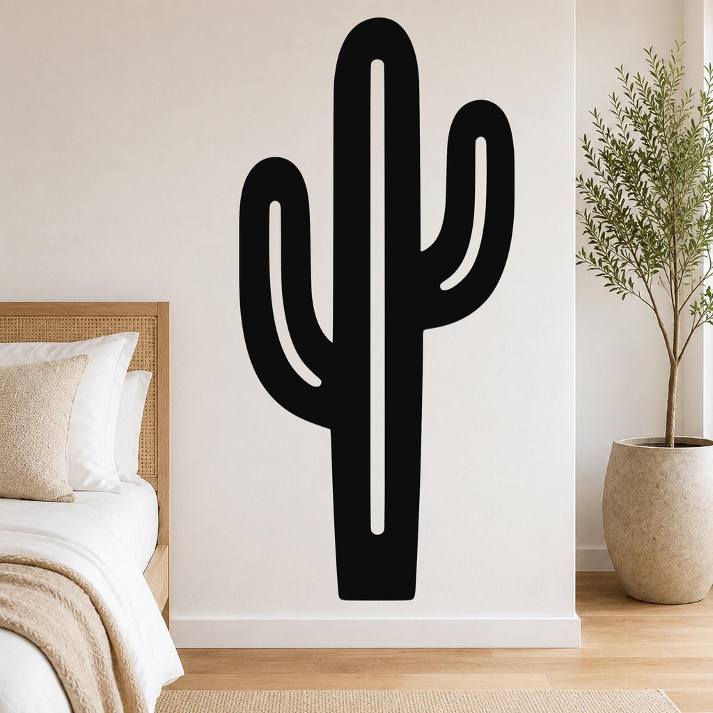 Black metal saguaro cactus wall art with cutout arms, mounted on a white bedroom wall above a bed.