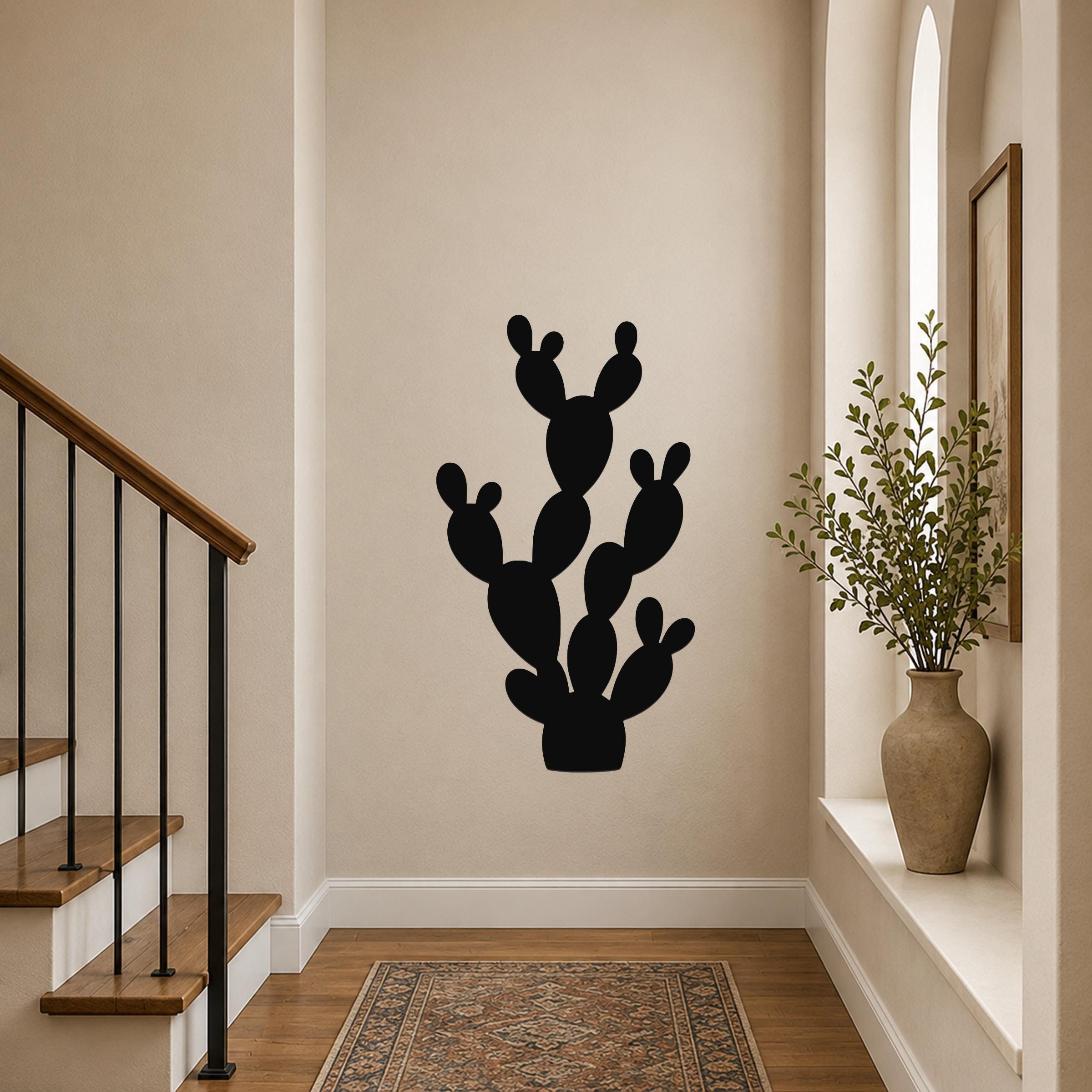 Black metal wall art in the silhouette of a prickly pear cactus, mounted on a hallway wall above a patterned rug.
