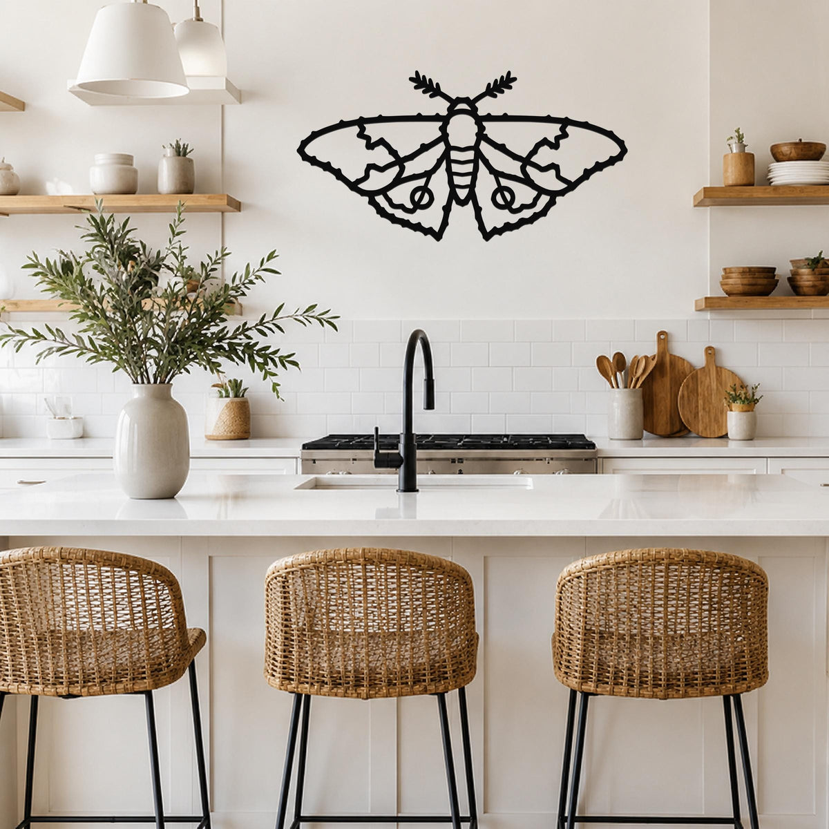 Black metal moth wall art with detailed wing cutouts, mounted on a kitchen wall above a white countertop.