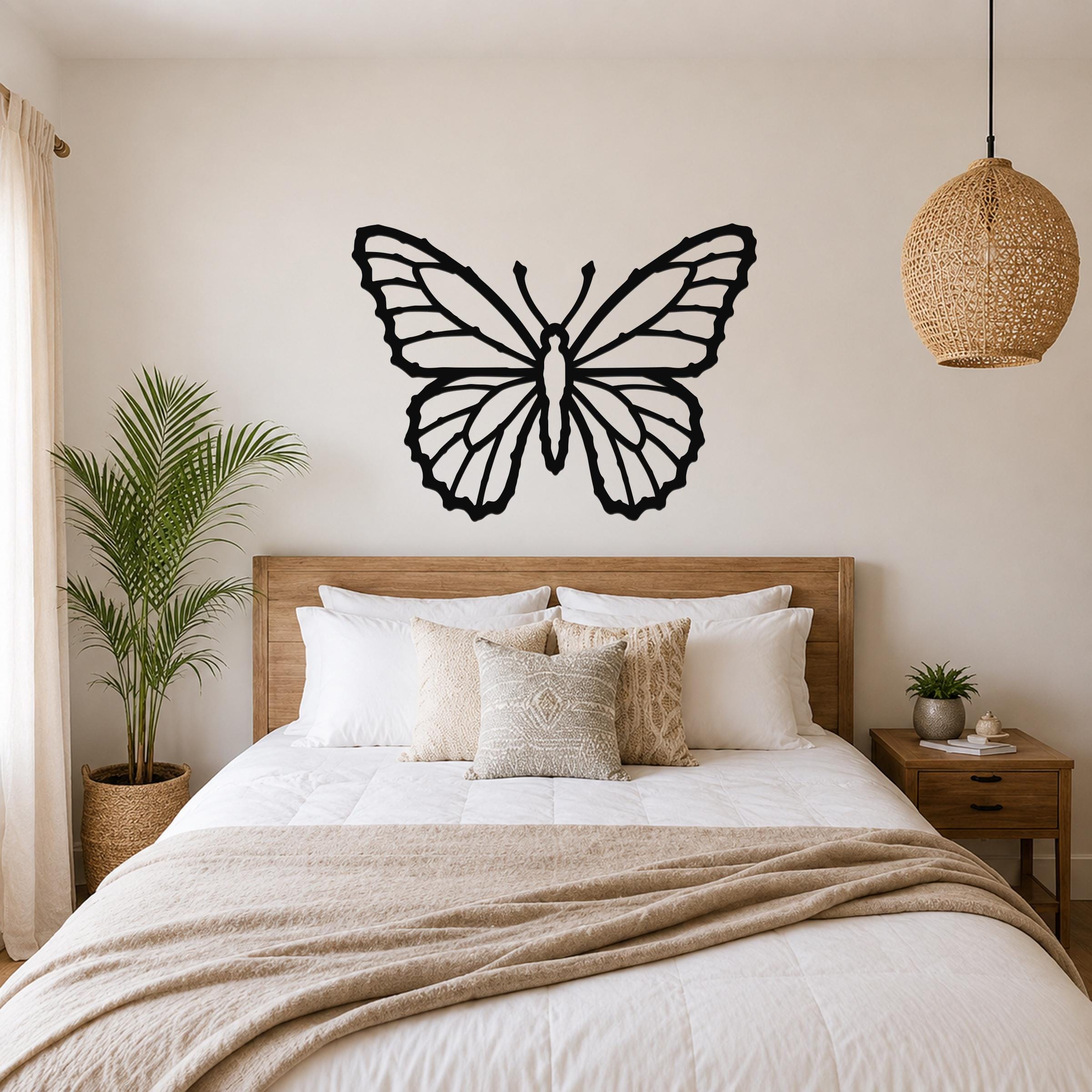 Black metal butterfly wall art with detailed wing cutouts, mounted above a wooden bed in a neutral bedroom.