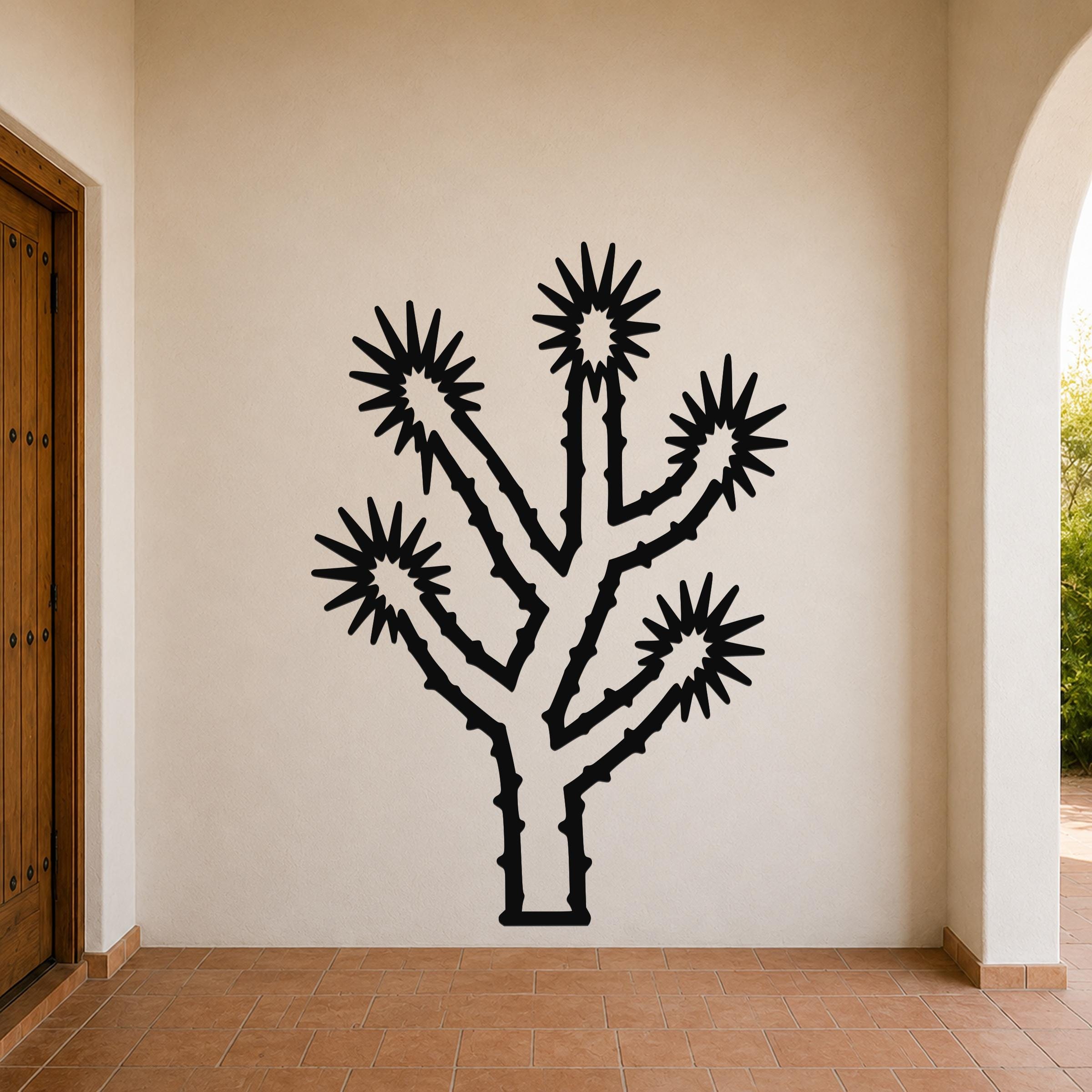 Black metal Joshua tree wall art with starburst flower cutouts, mounted on a beige stucco wall in a covered patio entryway.