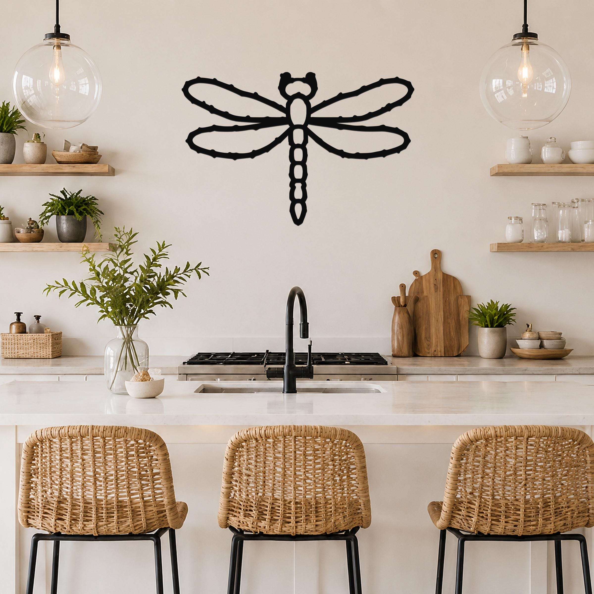 Black metal dragonfly wall art with detailed wing and body cutouts, mounted on a kitchen wall above a counter.